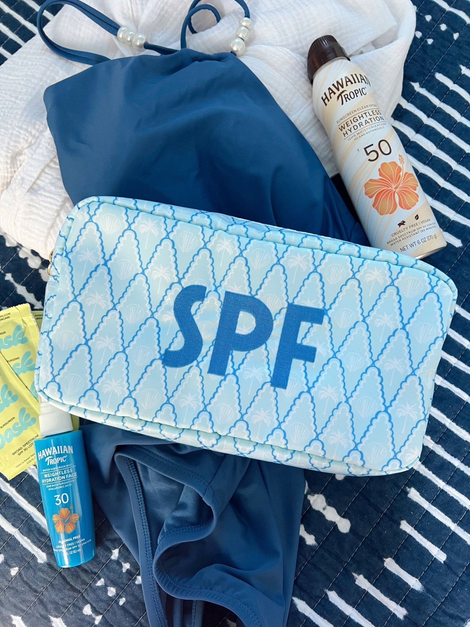 Light blue makeup bag with "SPF" text and palm tree pattern, displayed with sunscreen bottles and beach towels