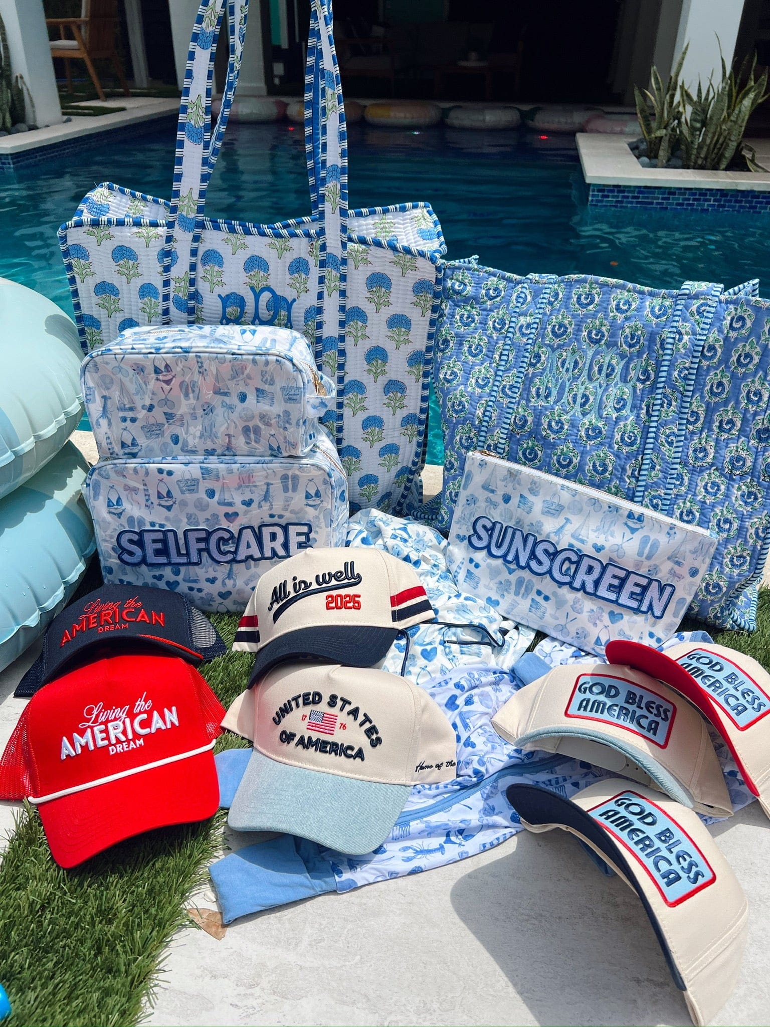 Blue and white patterned makeup bag with "SELF CARE" text, displayed poolside with matching coordinating accessories and patriotic hats.
