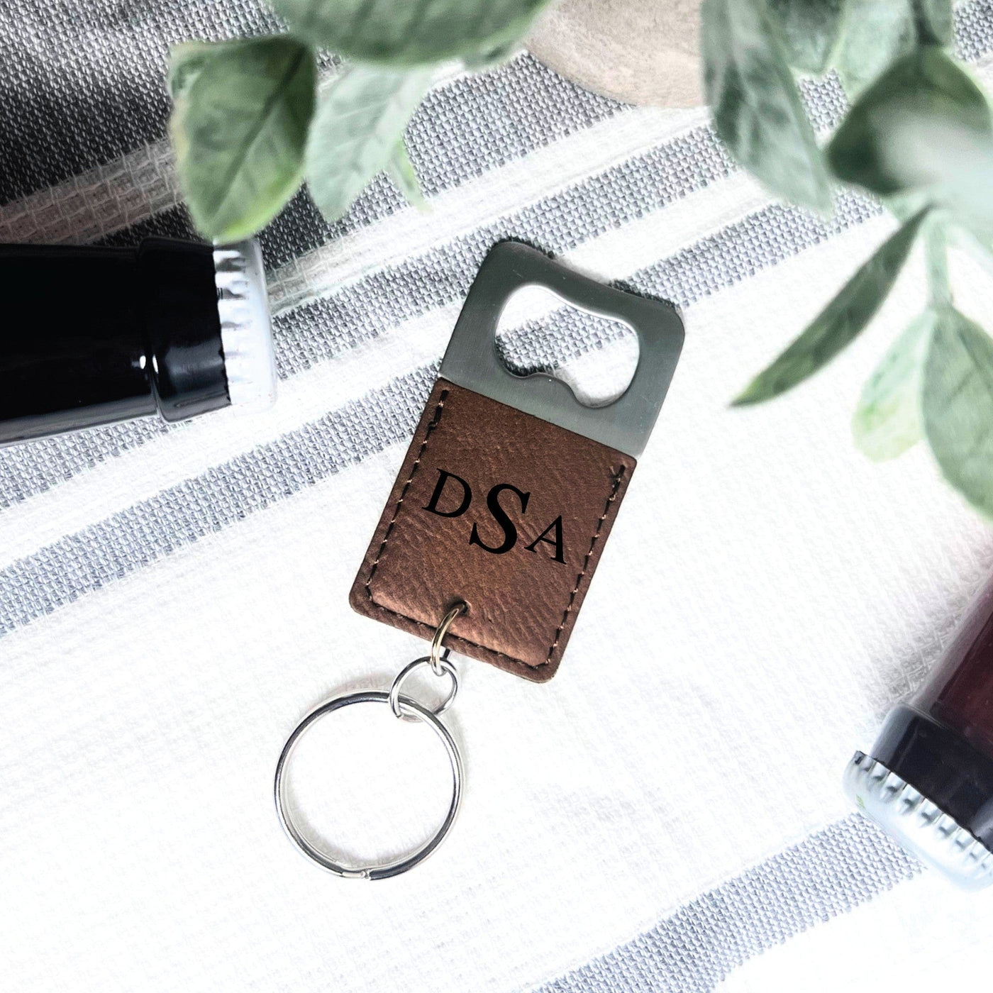 A personalized bottle opener keychain features a brown leatherette wrap around a silver metal bottle opener, attached to a silver key ring for convenient carrying.