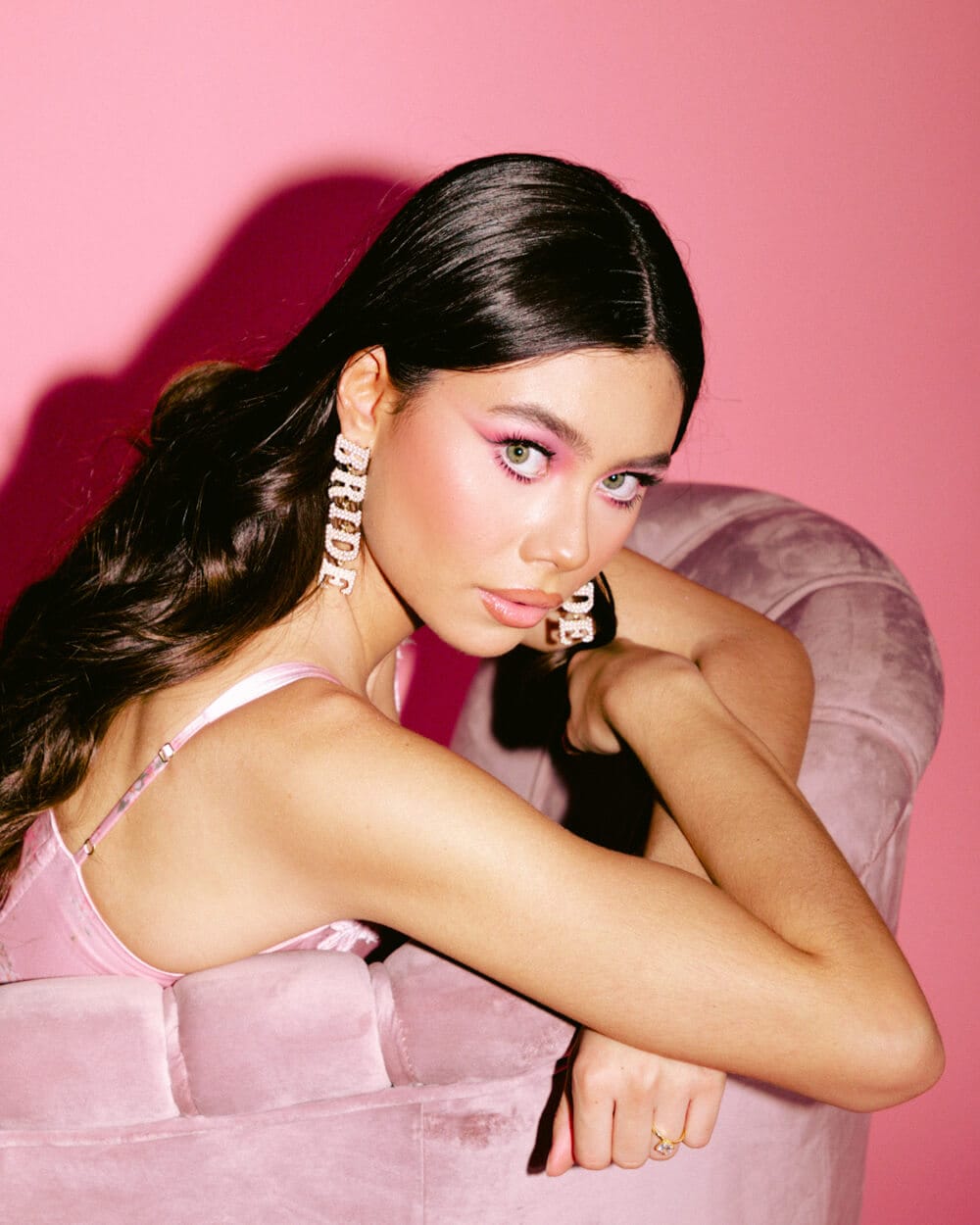 Woman wearing long pearl drop earrings with matching necklace against pink background.