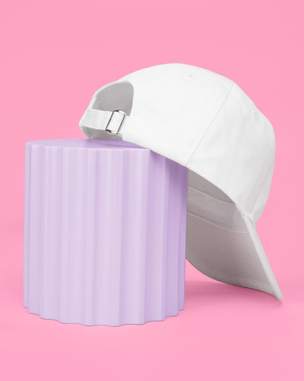 White cotton baseball hat with embroidered bride text and metal buckle back closure on pink background next to lavender cup.