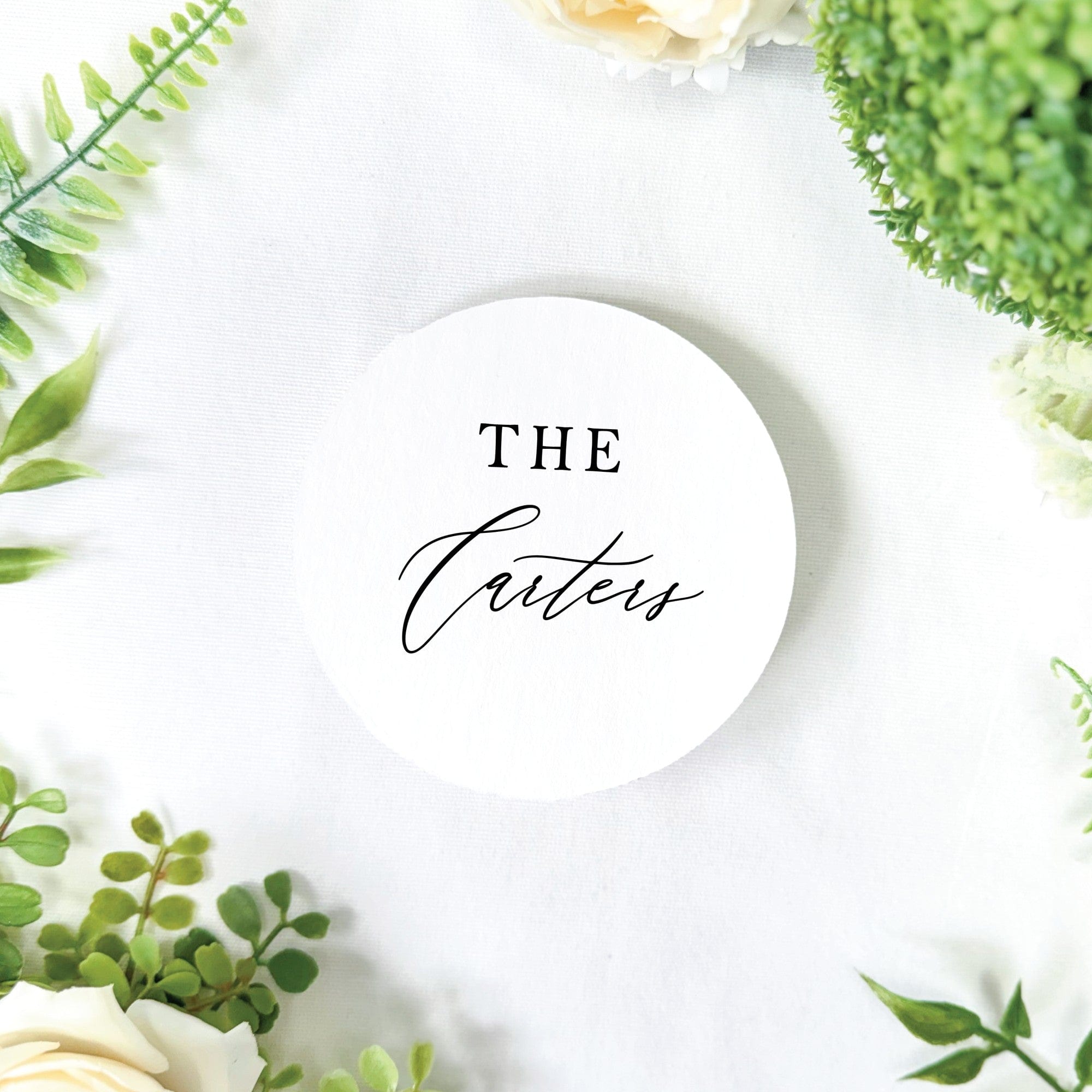 A white round personalized wedding sign or coaster with elegant black typography, perfect for event table decor.