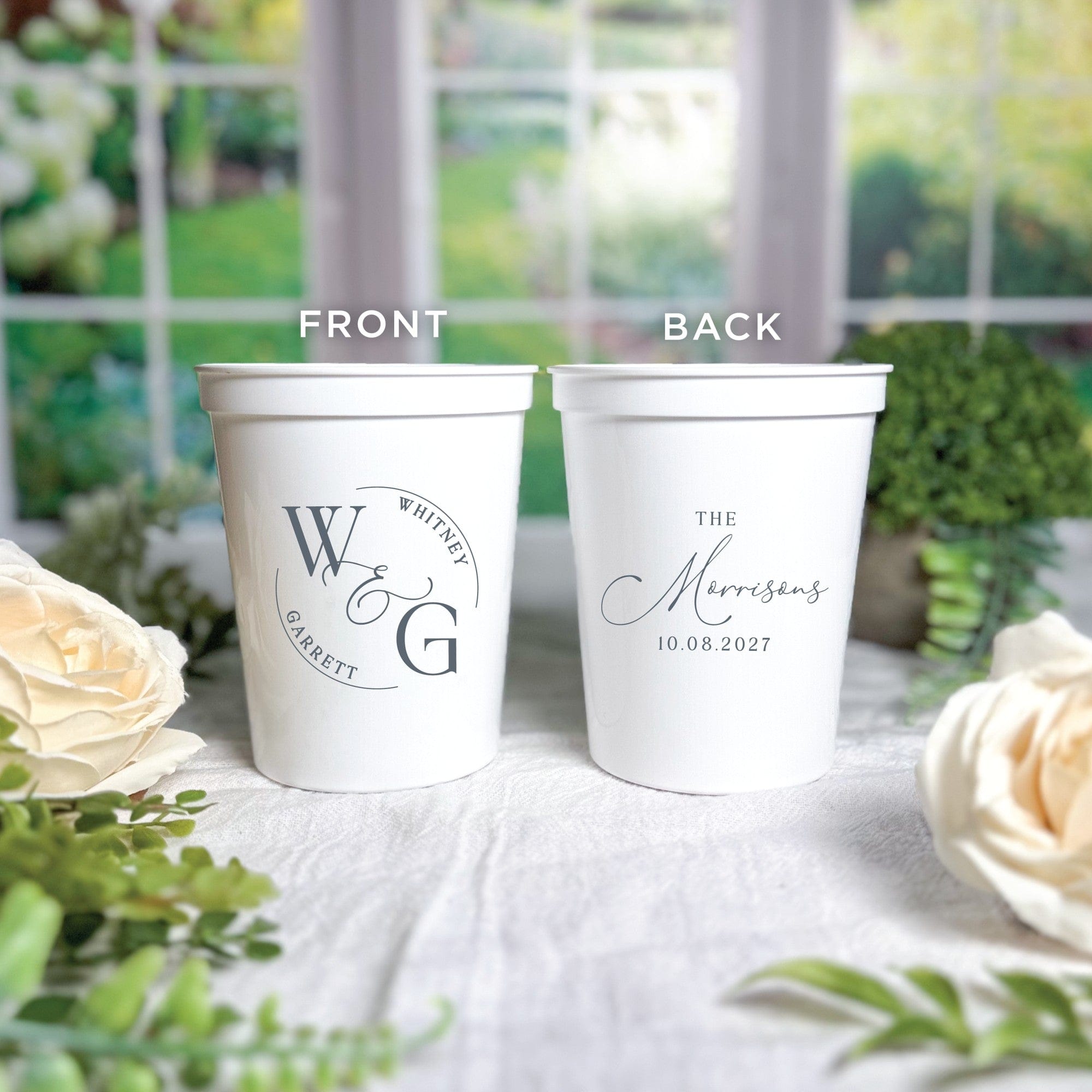 Two white reusable plastic wedding cups are shown, one with a personalized initial monogram design on the front and the other with a custom family name design on the back.