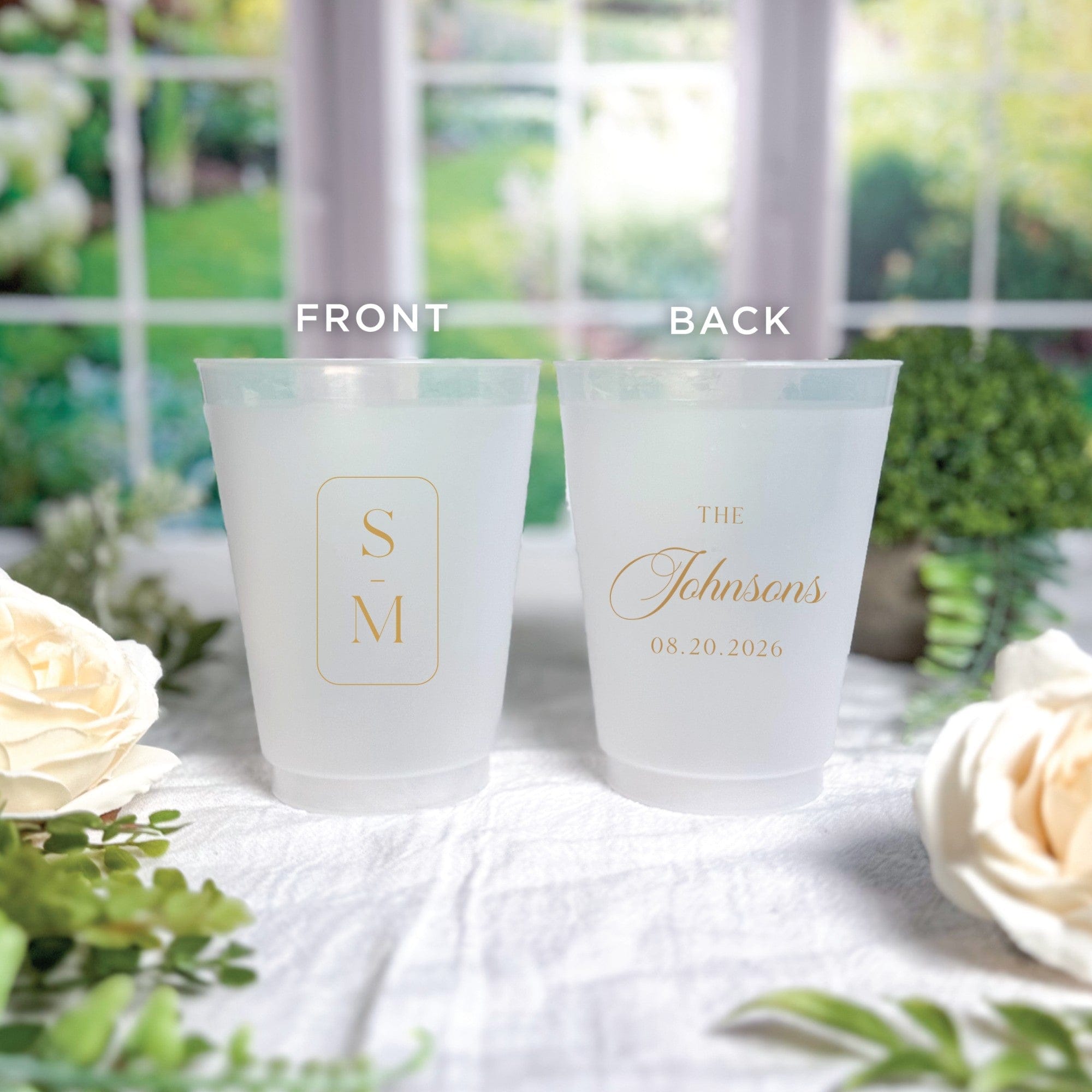 Two frosted plastic cups, personalized with elegant gold foil designs, are displayed as stylish wedding event decor.