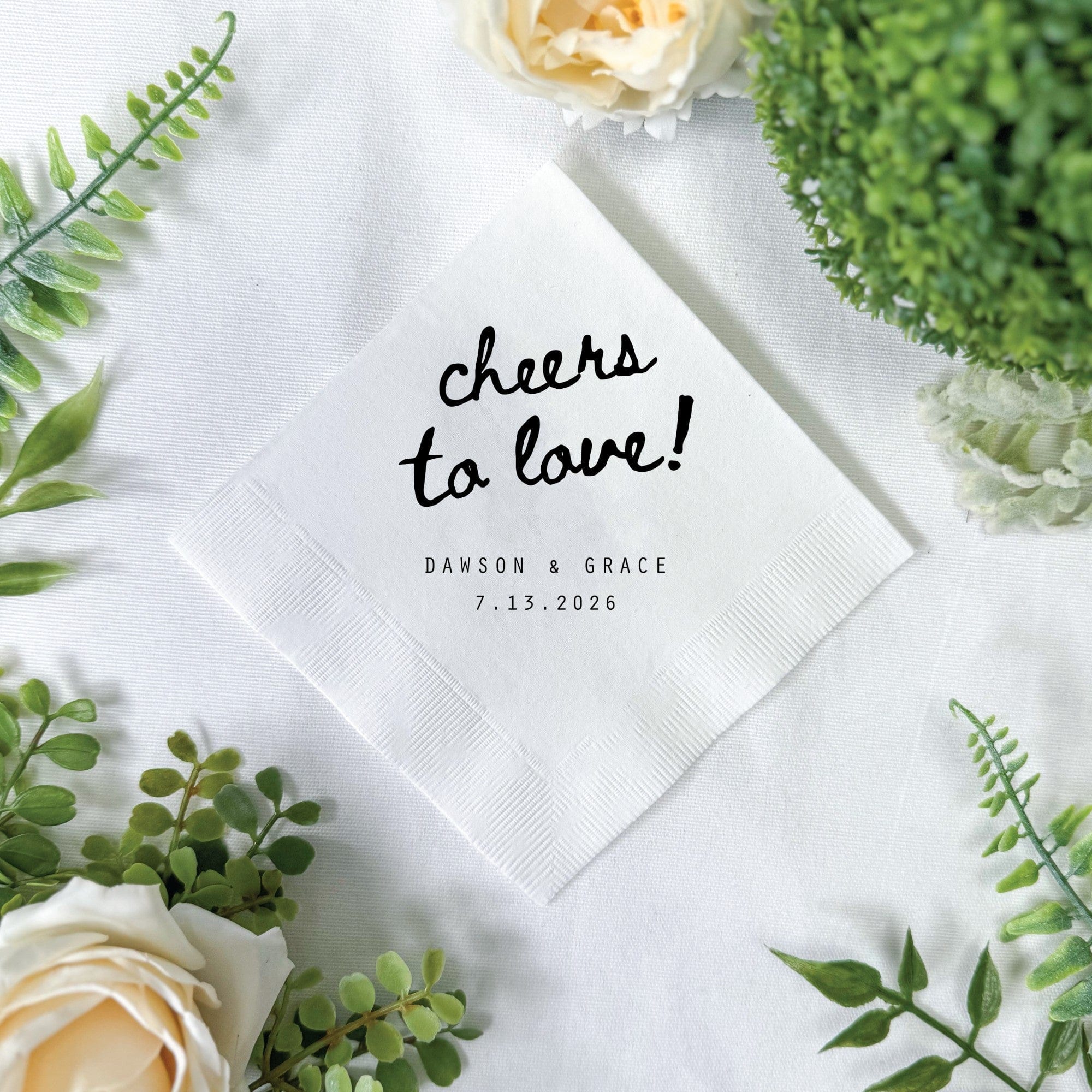 A white folded paper napkin features a custom black script design, ideal for wedding or event decor.