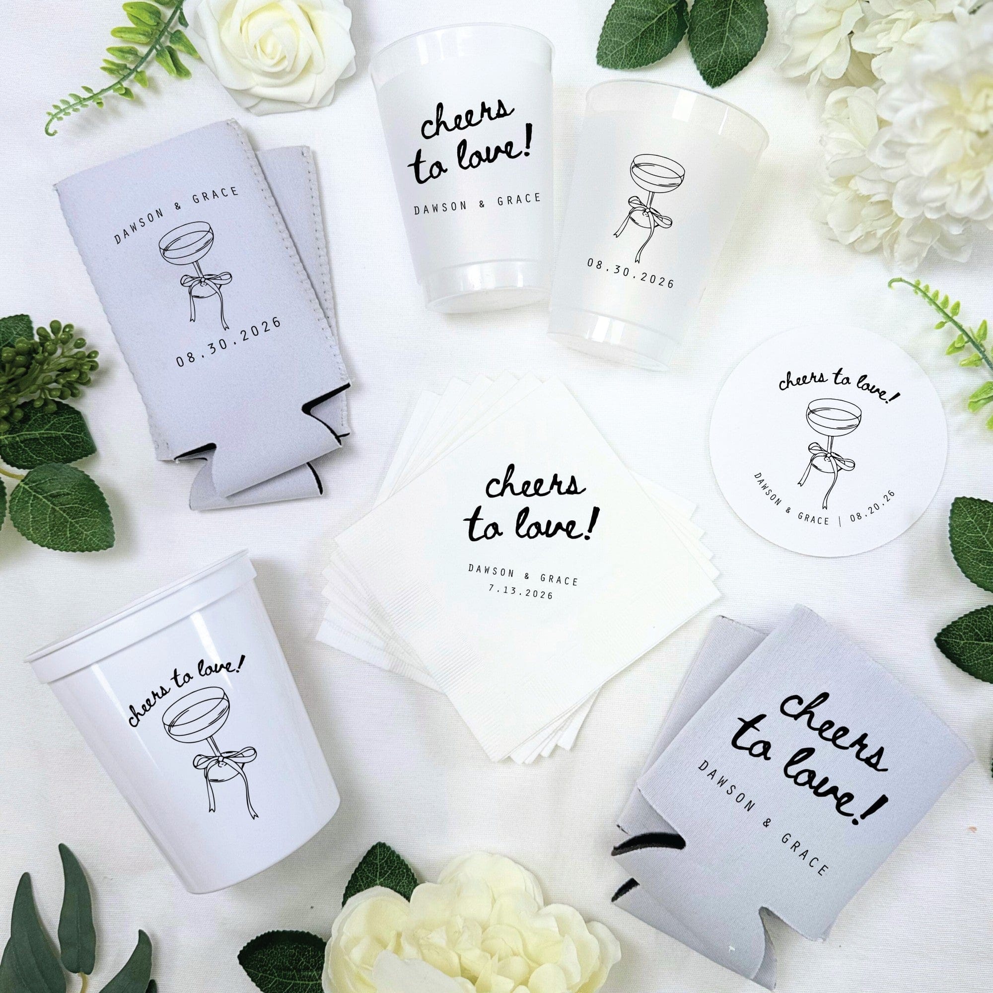 A collection of personalized wedding party supplies, including light gray neoprene can coolers, white frosted plastic cups, white stadium cups, white paper napkins, and a white round paper coaster, all featuring a black champagne glass illustration and celebratory phrase.