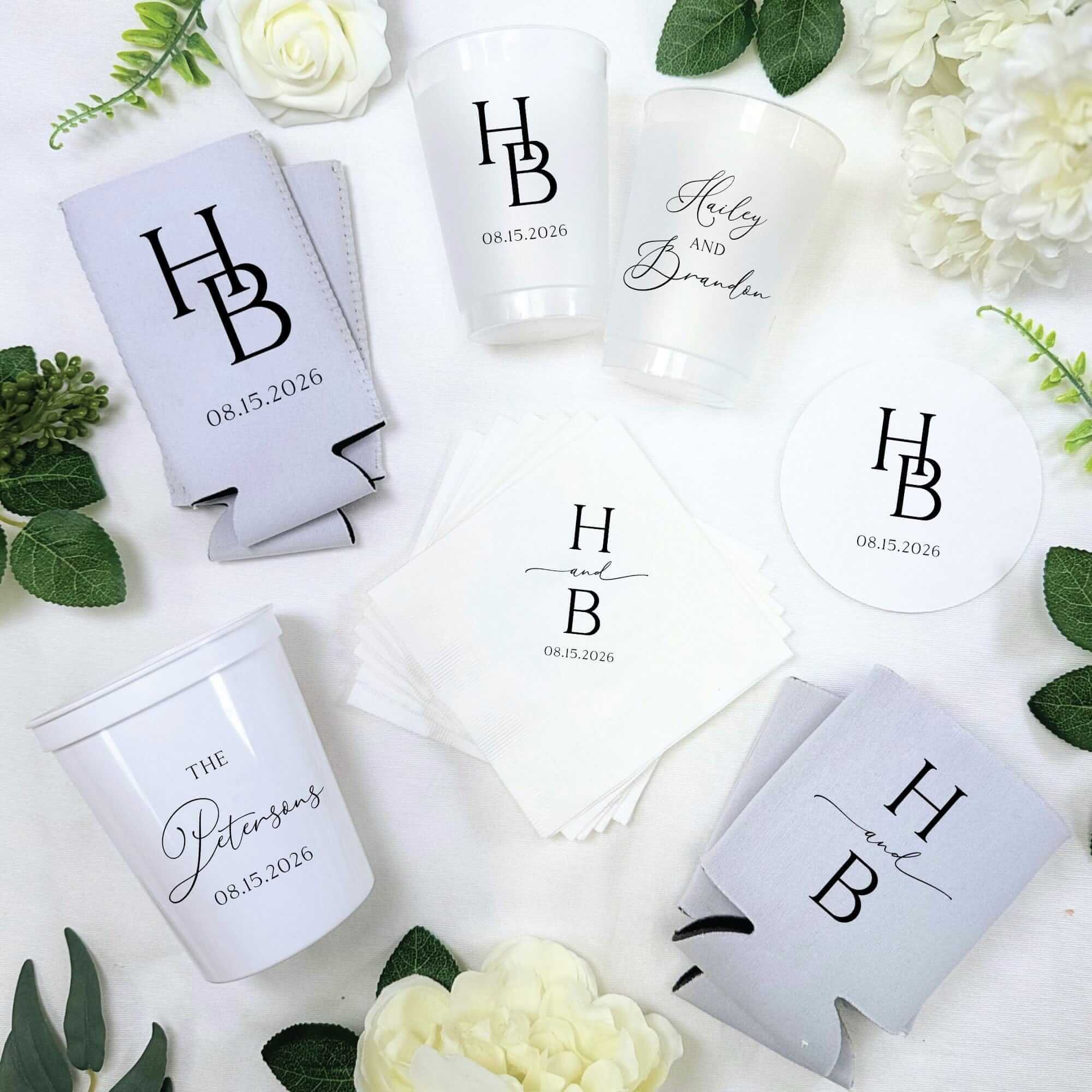 This collection features light grey neoprene can coolers, frosted clear and white opaque plastic cups, white paper napkins, and white round paper coasters, all custom printed for a wedding or special event.