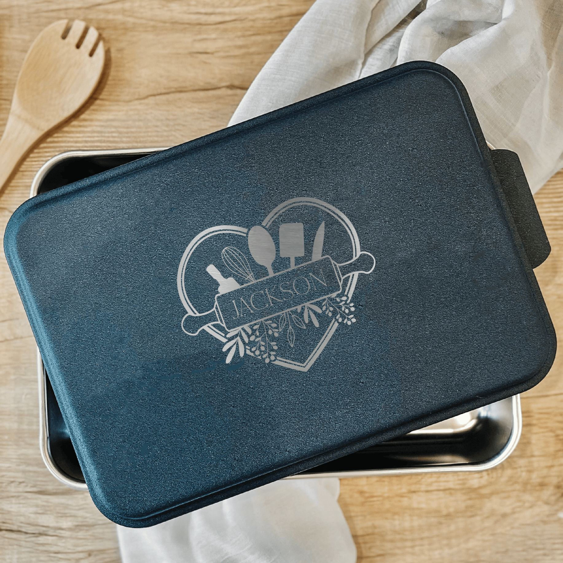 Dark teal rectangular cake pan with silver engraved last name and decorative heart design on lid.