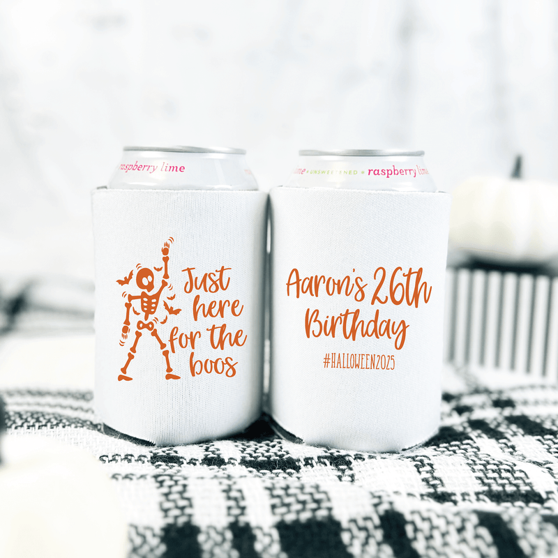 White can coolers with orange text reading "just here for the boos" and "Aaron's 26th Birthday" with hashtag, displayed on patterned fabric.