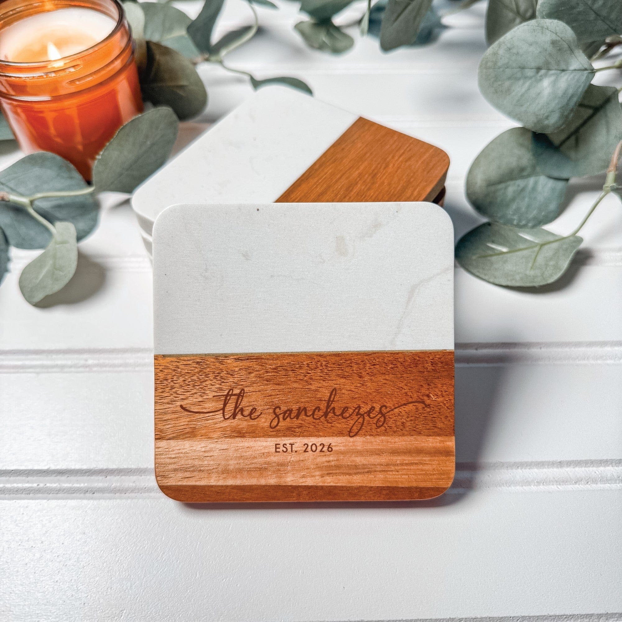 A square wedding coaster featuring a two-toned design with white marble on the top half and light brown wood on the bottom half, intended for event decor or favors.