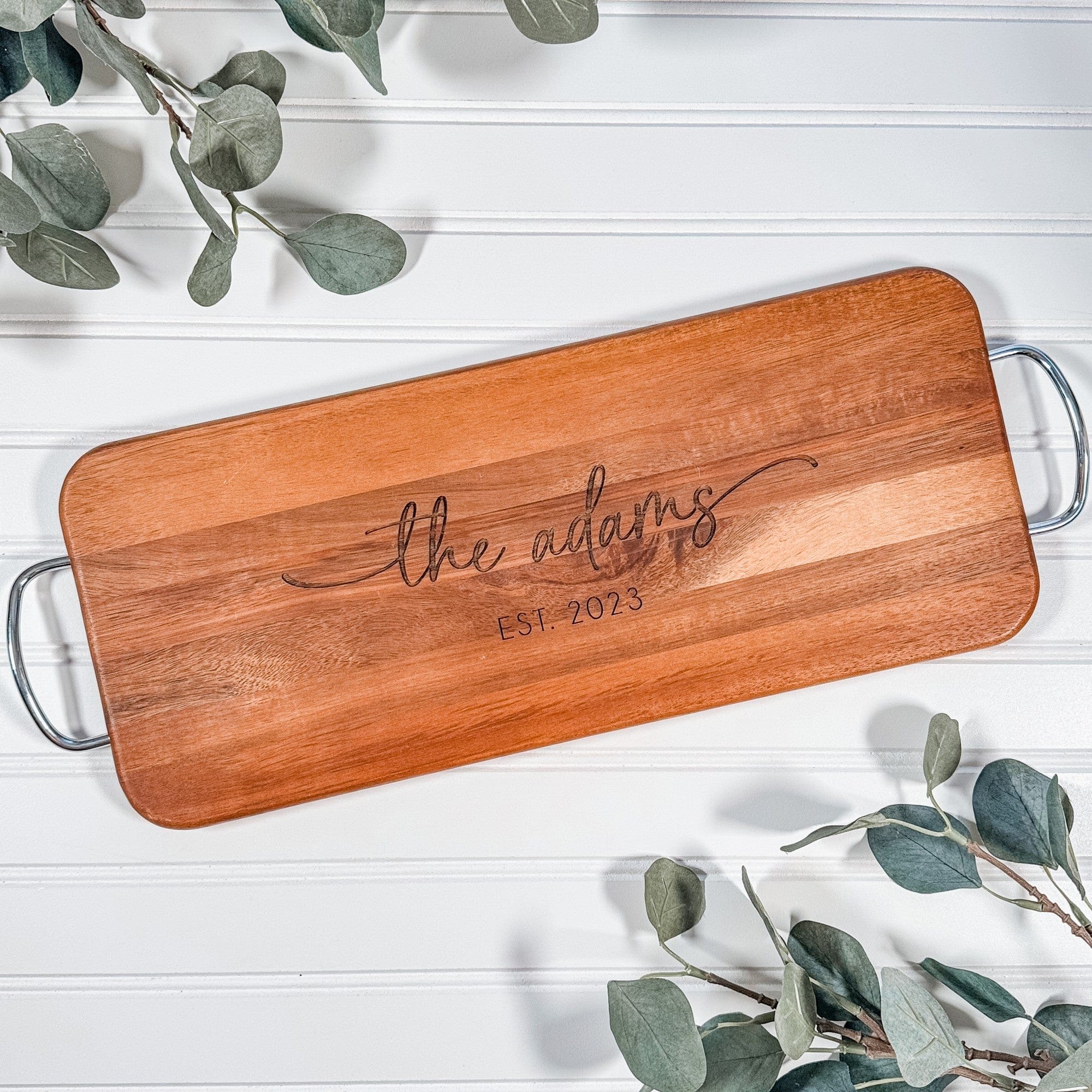 A rectangular wooden serving board with integrated metal handles features a custom engraved design, ideal for a wedding or anniversary gift.