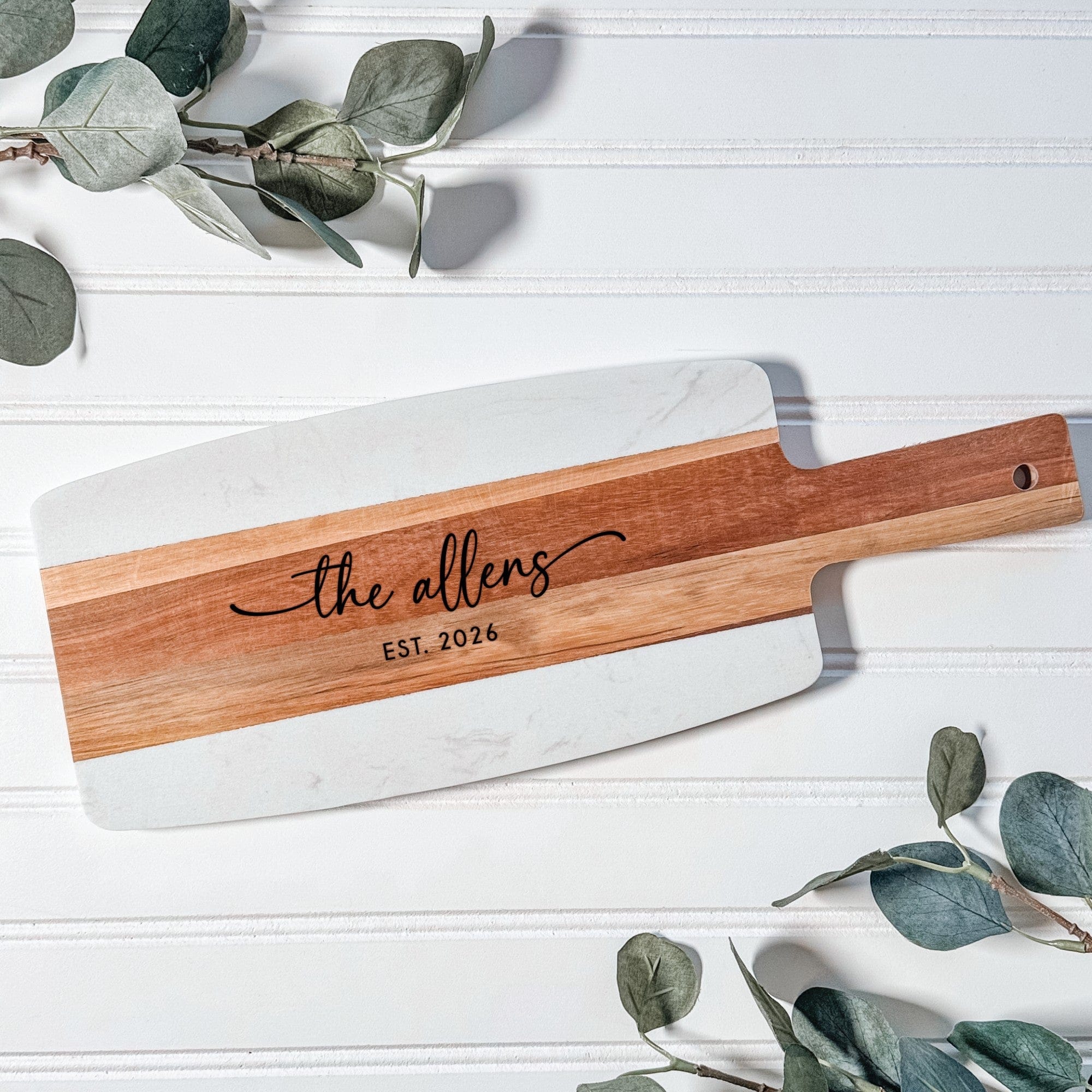 A personalized rectangular serving board crafted from white marble and rich brown wood, featuring a handle with a hanging hole, ideal for a wedding or anniversary gift.