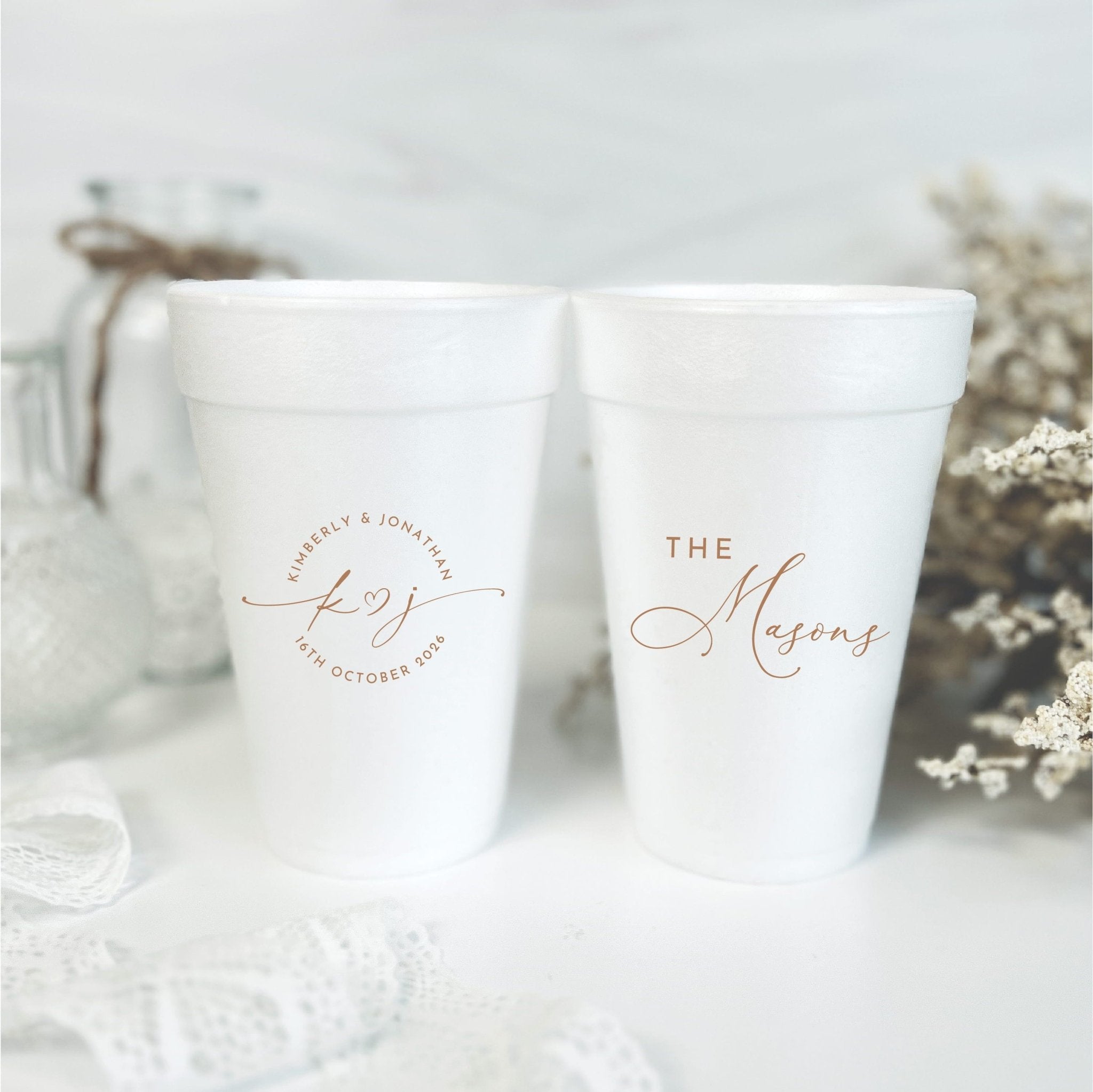 Two white foam cups with rose gold personalized text, one reading "The Hayzens" and the other with a circular wedding date design