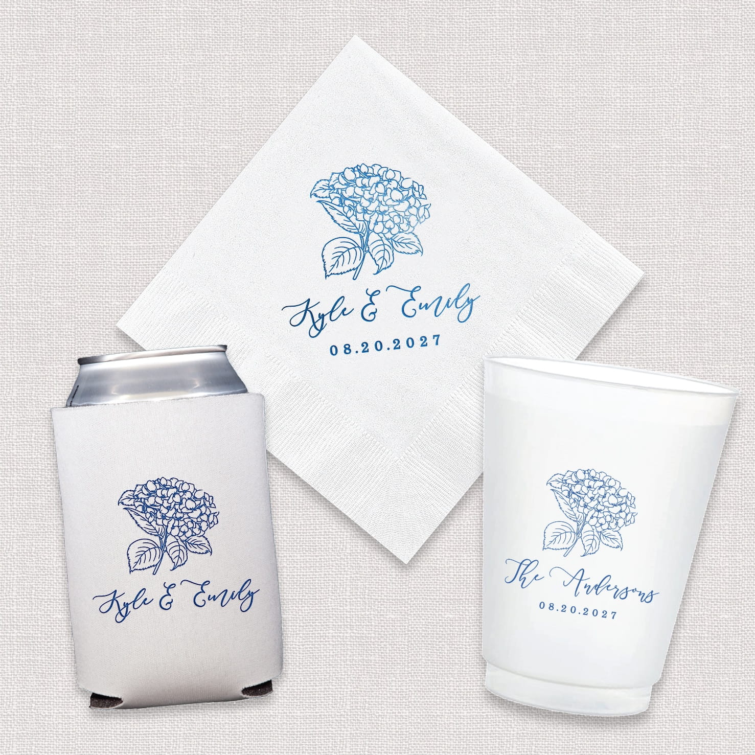 A complete Hydrangea wedding bundle featuring personalized cocktail napkins, frosted shatterproof cups, and neoprene can coolers with a hydrangea floral design, arranged as a coordinated set.