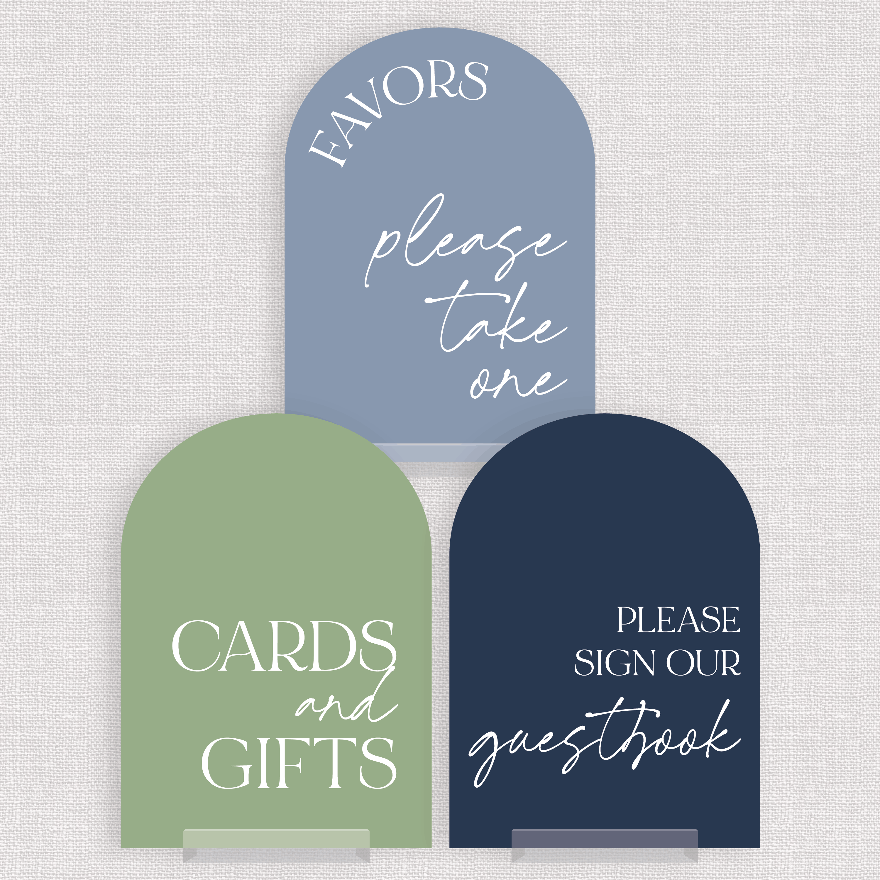 Three arched acrylic wedding signs in dusty blue, sage green, and navy displayed on clear stands against a neutral linen background, reading Favors Please Take One, Cards and Gifts, and Please Sign Our Guestbook.