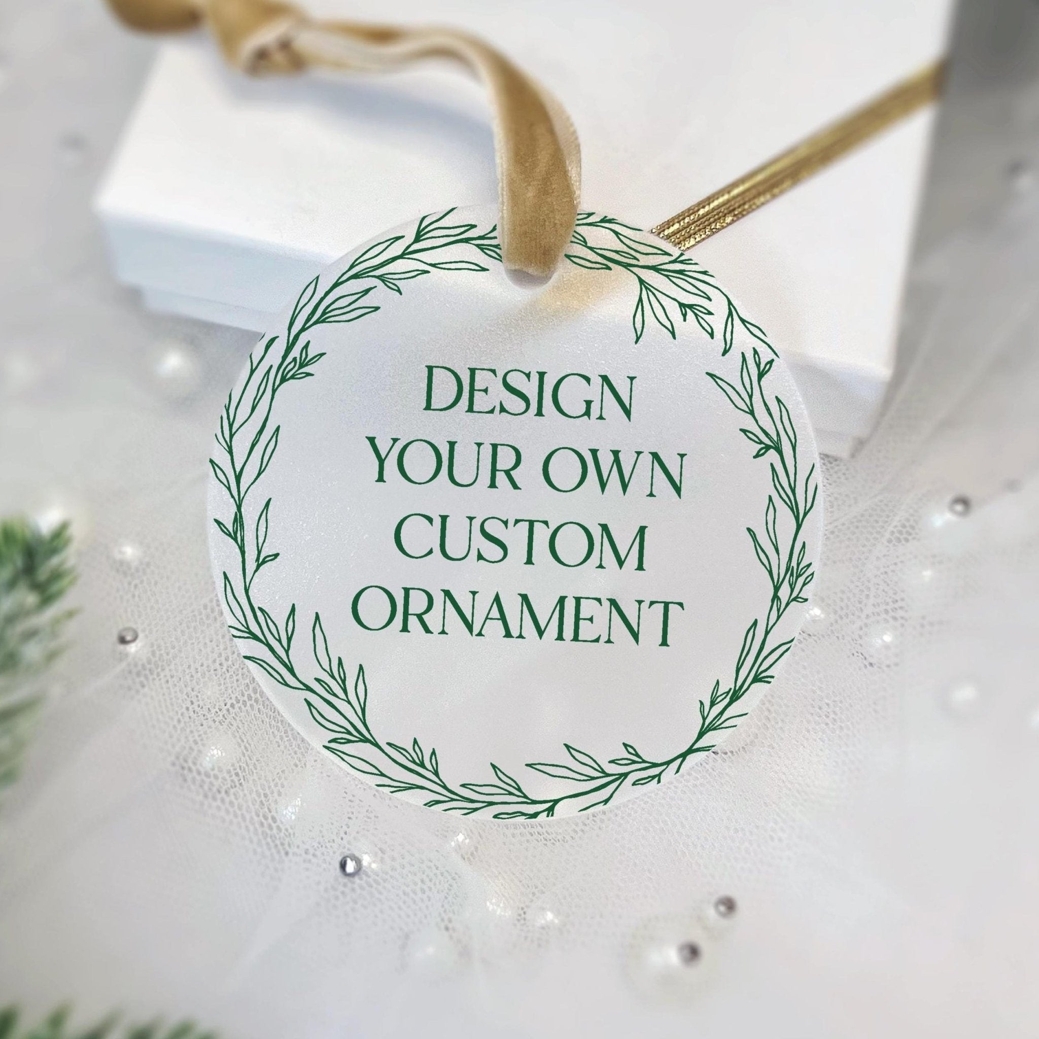 Round acrylic ornament with green leaf wreath border and "Design Your Own Custom Ornament" text, attached with twine loop.