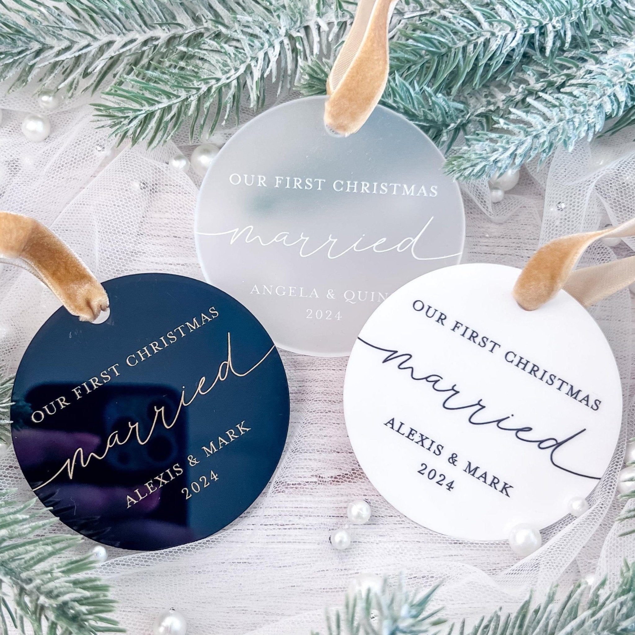 Personalized round acrylic Christmas ornaments in navy blue and white with "Our First Christmas Married" text and couple names, displayed with gold ribbon and evergreen branches.
