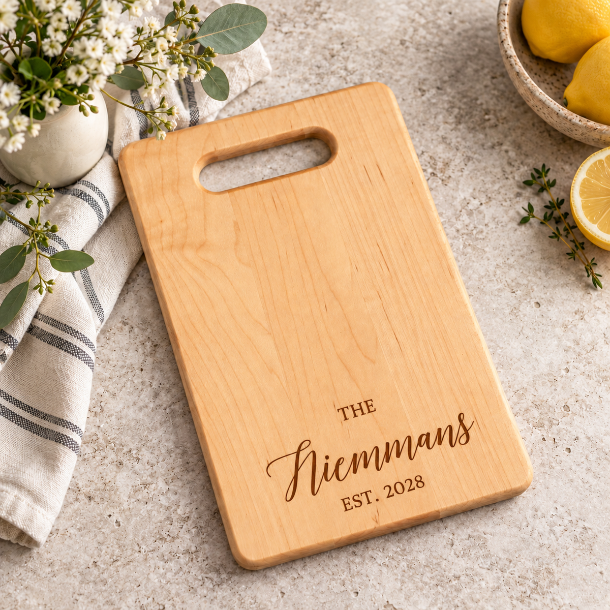 Personalized maple cutting board with engraved Niemmans family name and established year 2028, featuring a handle cutout and natural wood grain.