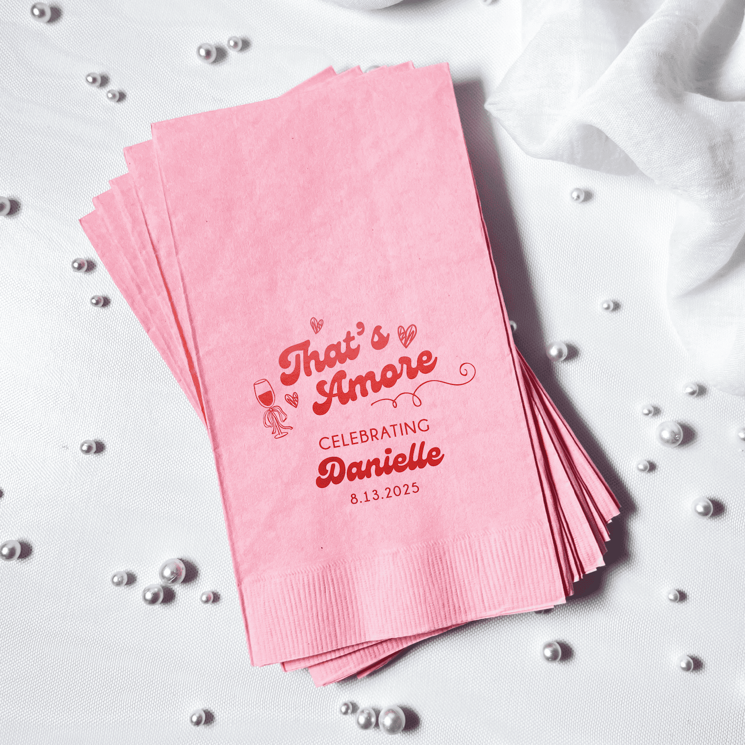 Stack of pink napkins with red foil-stamped text reading "That's Amore" and "Celebrating Danielle 8.13.2023"