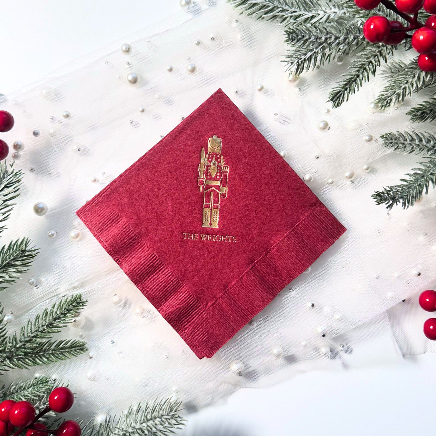 A folded deep red paper napkin features a gold foil nutcracker design, perfect for a festive holiday or Christmas party event.