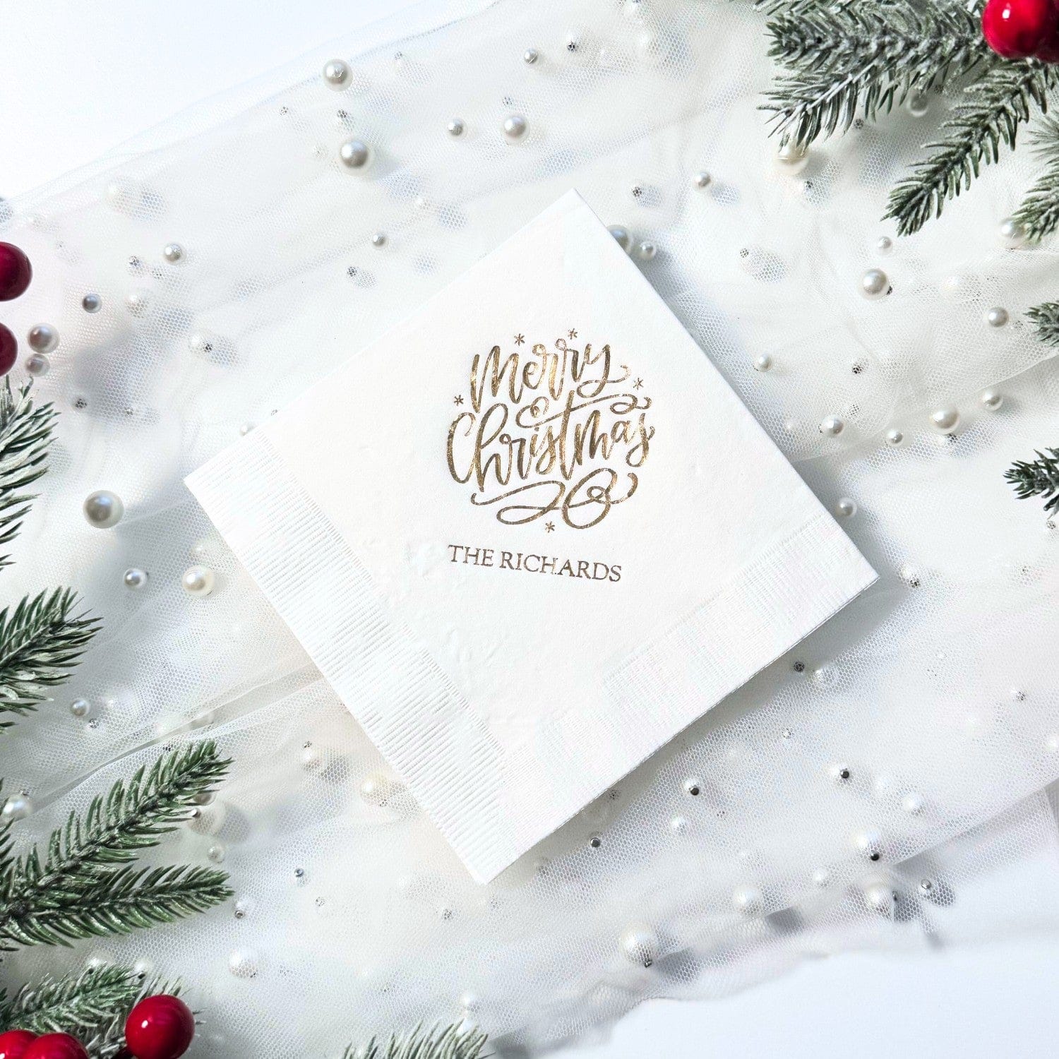 A white folded paper napkin featuring elegant gold foil script, suitable for a Christmas party or holiday event.