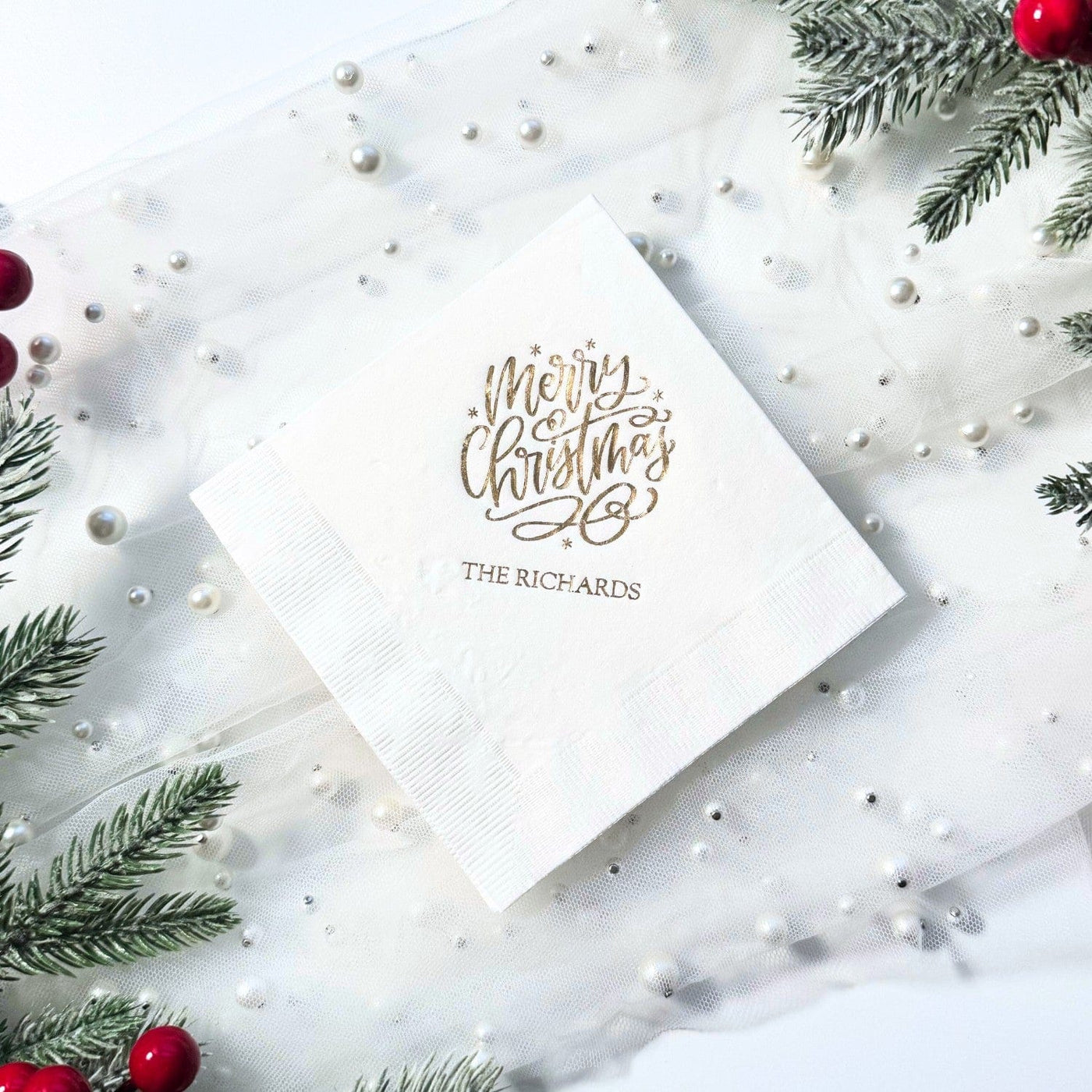 A white folded paper napkin featuring elegant gold foil script, suitable for a Christmas party or holiday event.