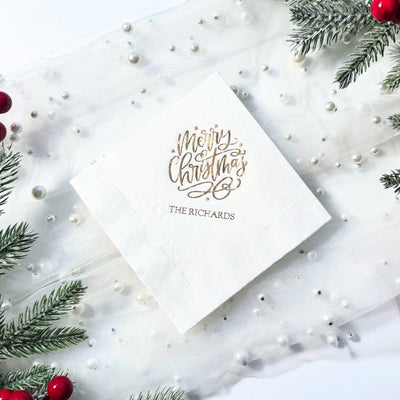 A white folded paper napkin featuring elegant gold foil script, suitable for a Christmas party or holiday event.