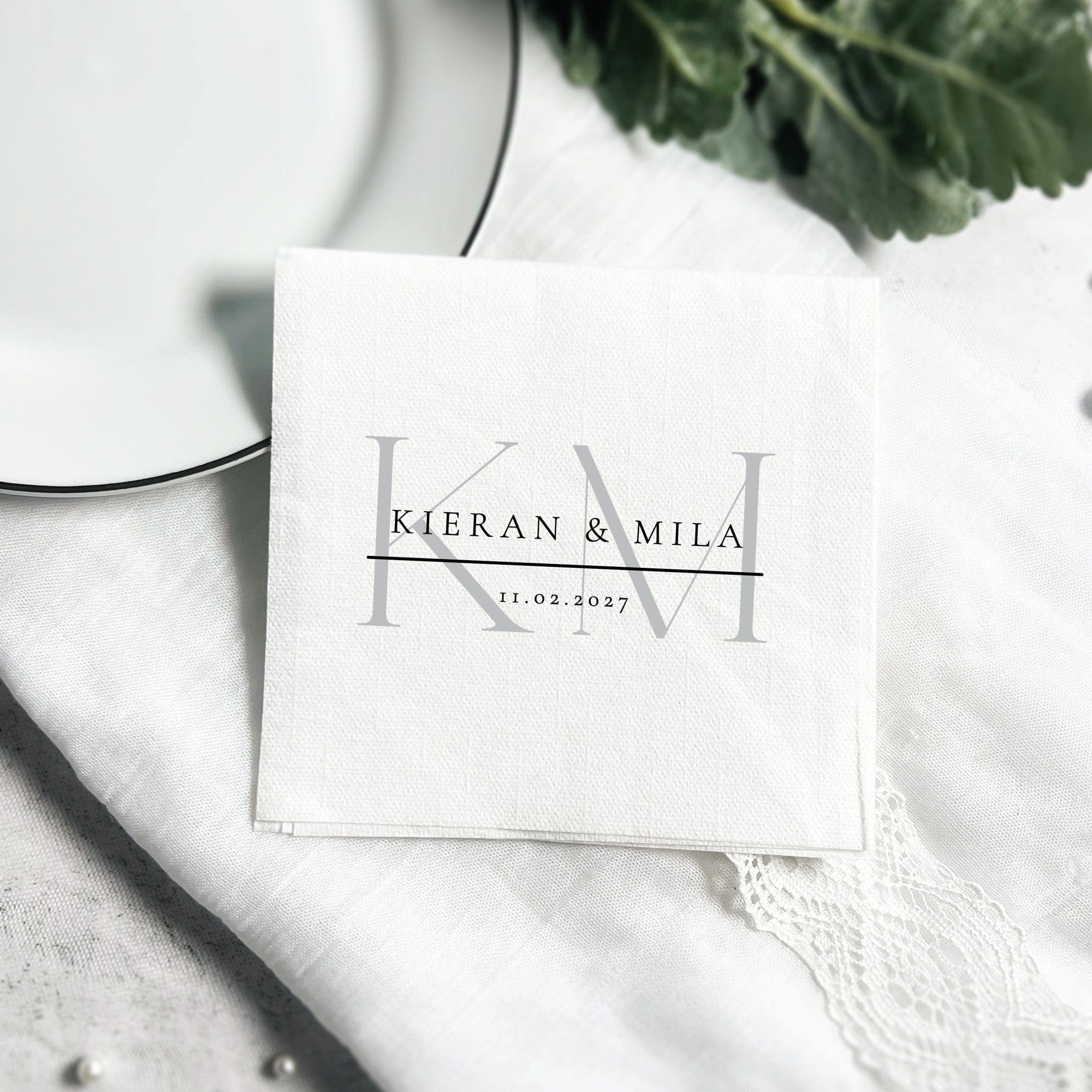 A white folded paper napkin for a wedding features an elegant custom print with prominent gray initial letters, designed to personalize event decor.