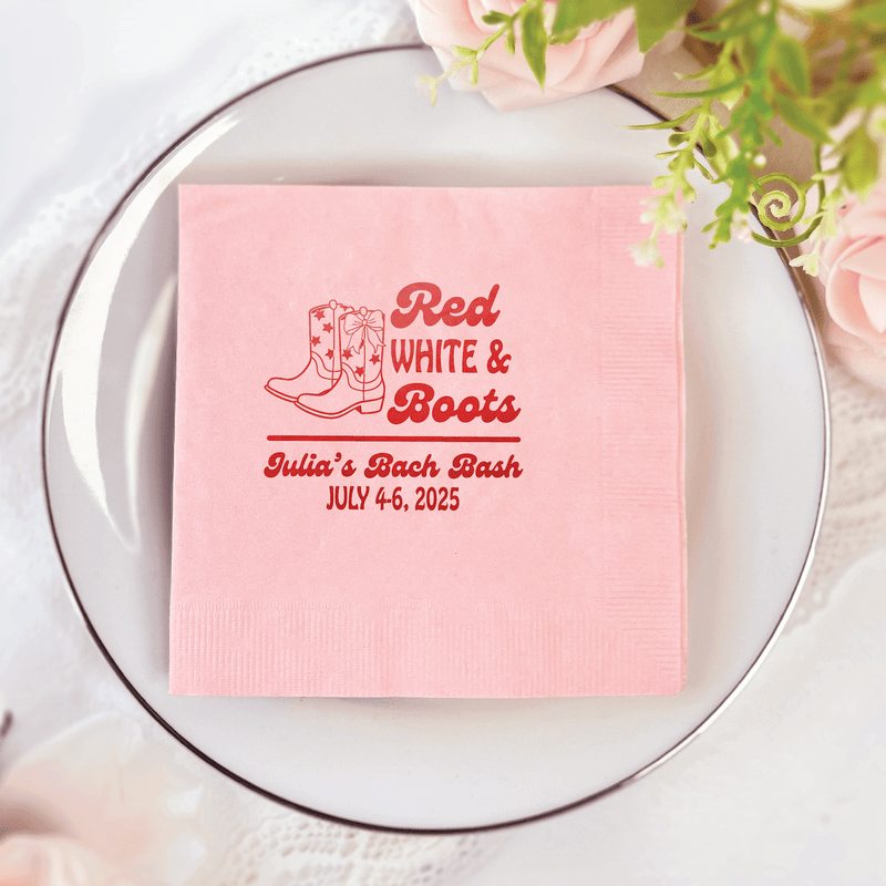 Pink cocktail napkin with red foil stamped cowboy boots design and "Red White & Boots" text, personalized with event details.
