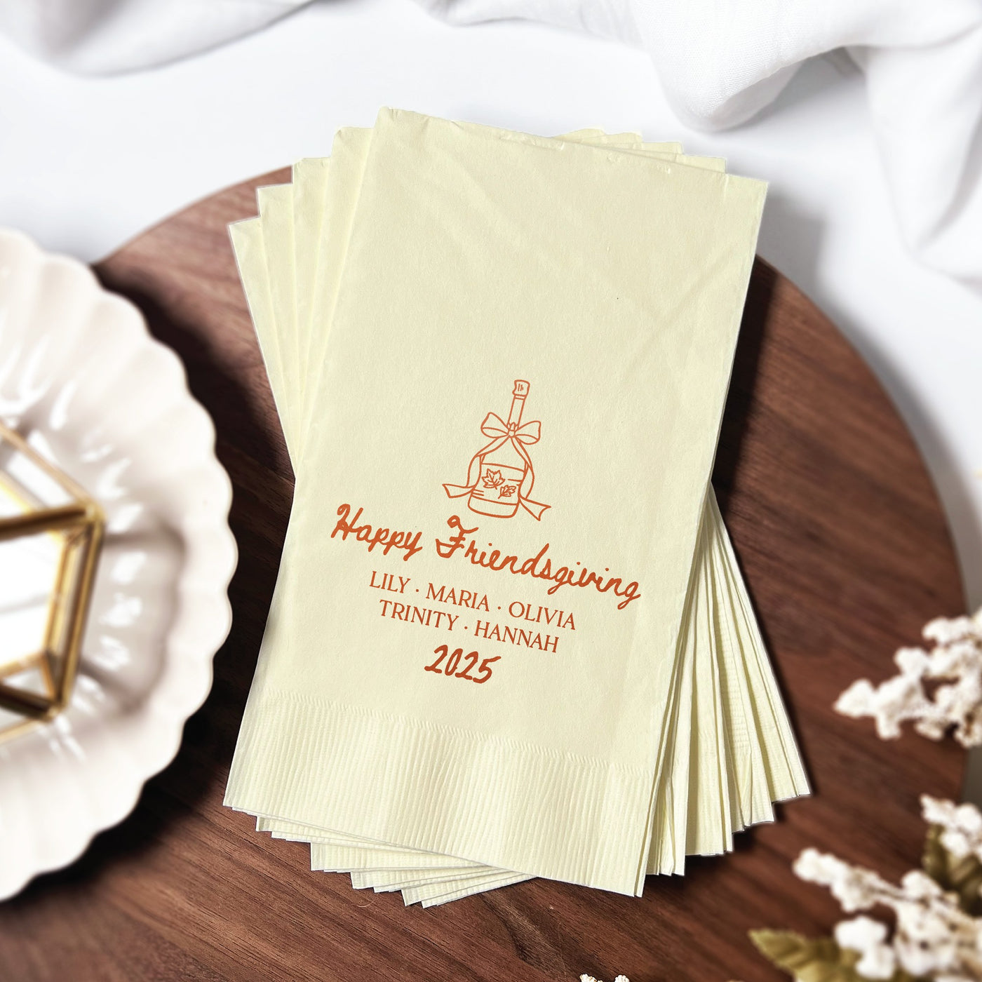 A stack of personalized pale yellow paper cocktail napkins, featuring a champagne bottle with autumn leaves illustration, suitable for a Friendsgiving or fall-themed event.