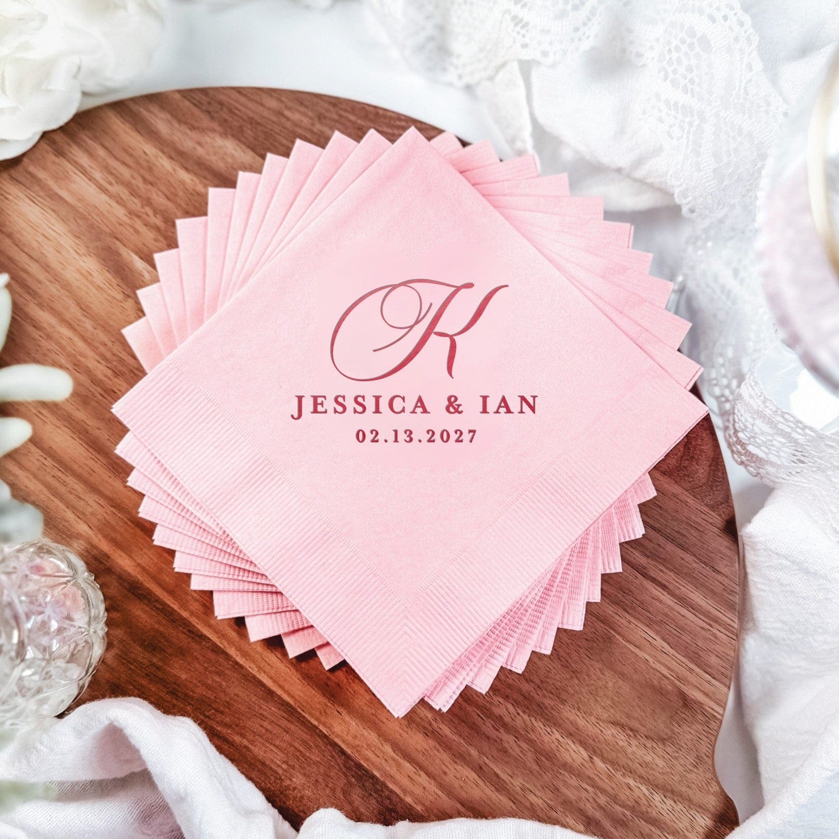 A stack of light pink disposable paper napkins, personalized with a dark pink initial and text, suitable for a wedding or special event.