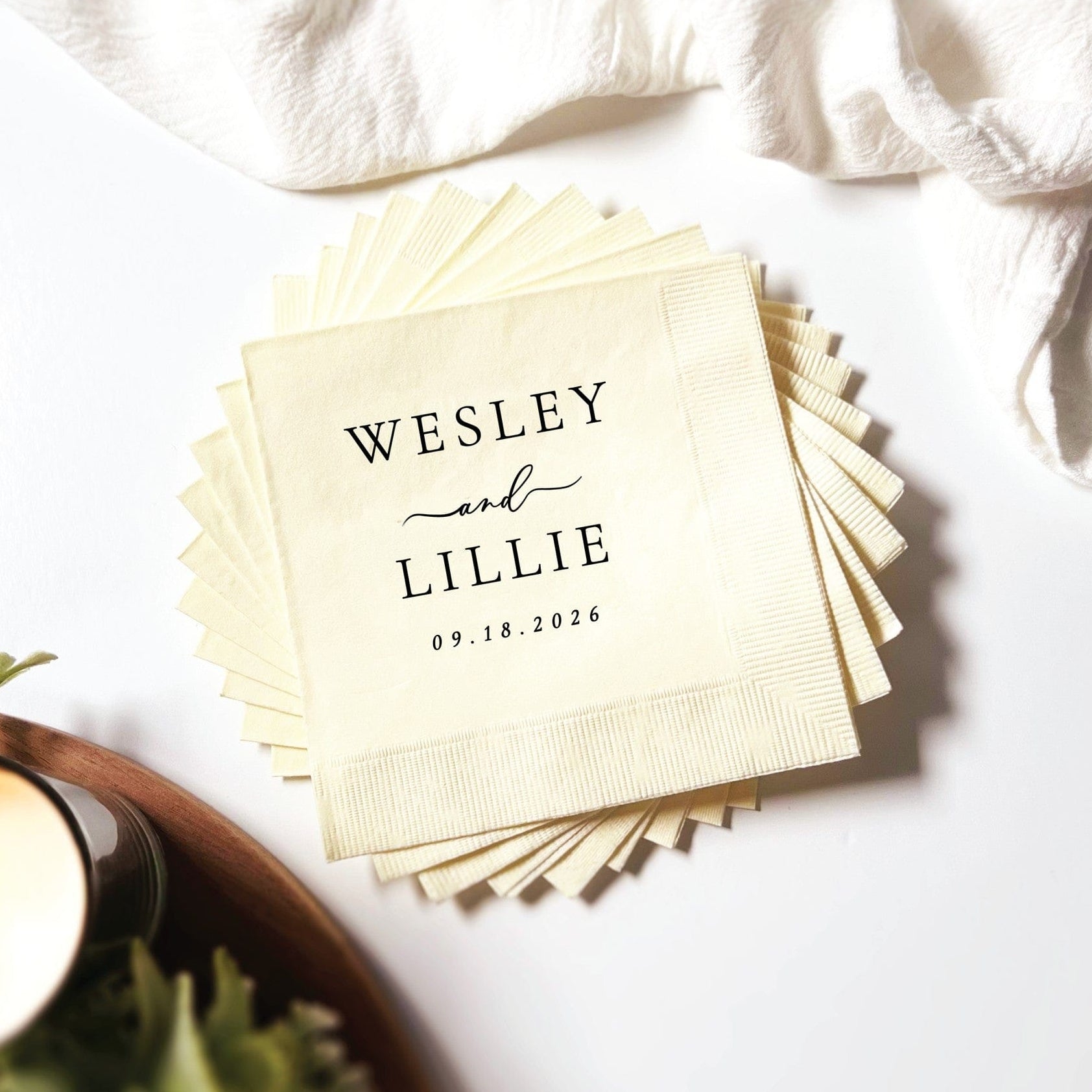 A fanned stack of cream-colored textured paper napkins personalized with custom black text, suitable for wedding or special event decor.