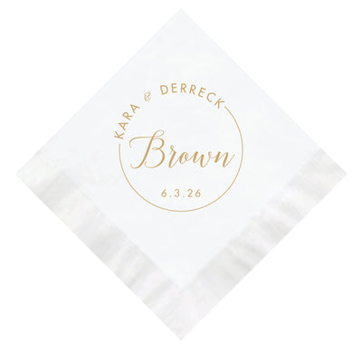A white disposable wedding napkin featuring a custom gold foil design with a circular border and elegant script typography for a personalized touch.
