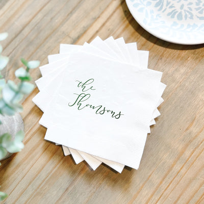 A stack of white paper wedding napkins personalized with custom script lettering in emerald green, suitable for a wedding or special event.