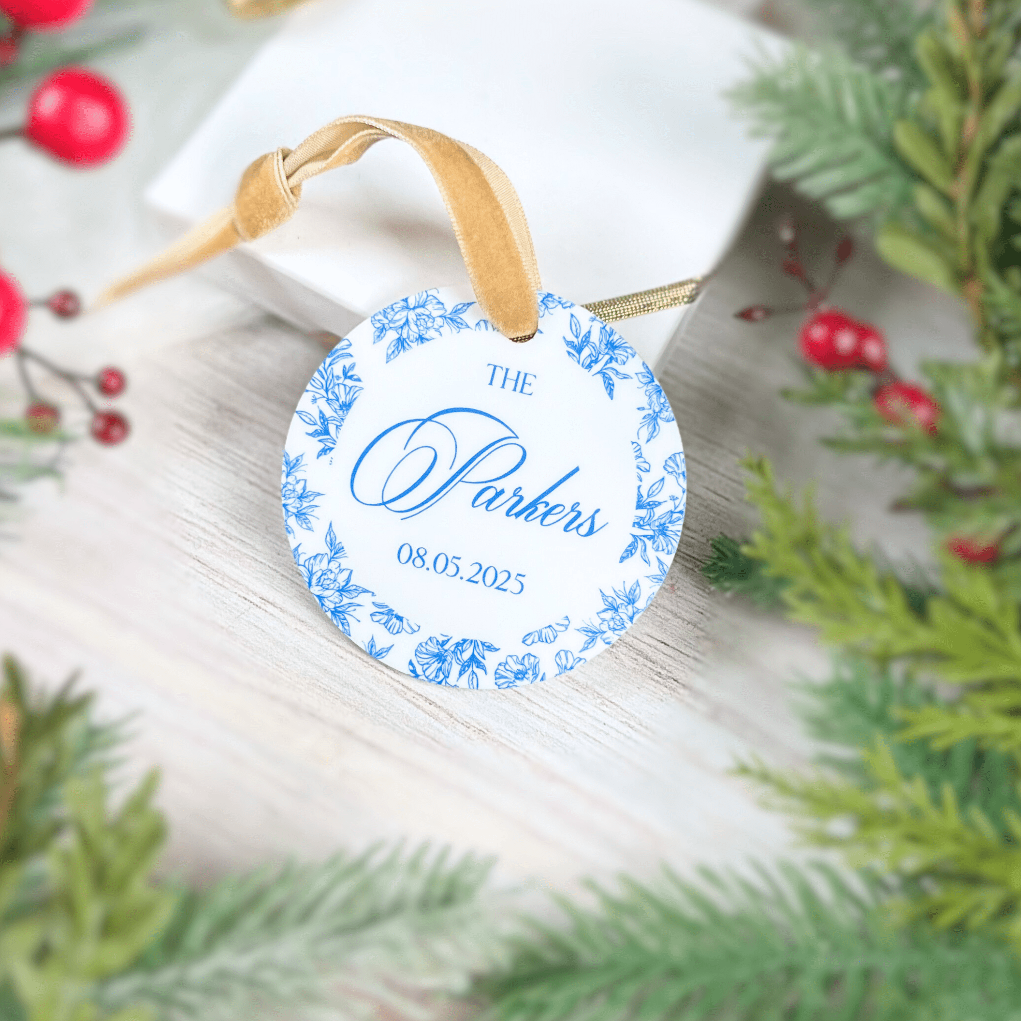 Round acrylic ornament with blue toile floral border and "The Parkers 08.05.2023" personalized text, tied with tan ribbon.