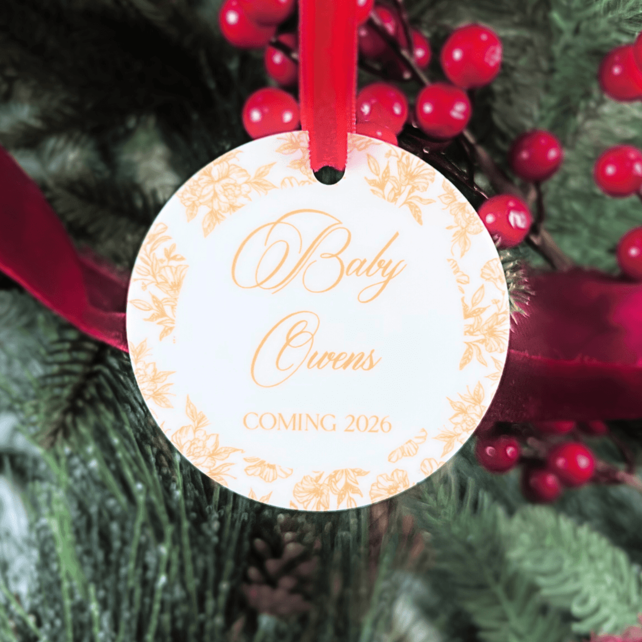 White circular acrylic ornament with peach toile pattern border and text reading "Baby Ovaries Coming 2026" in script, hanging from red ribbon.