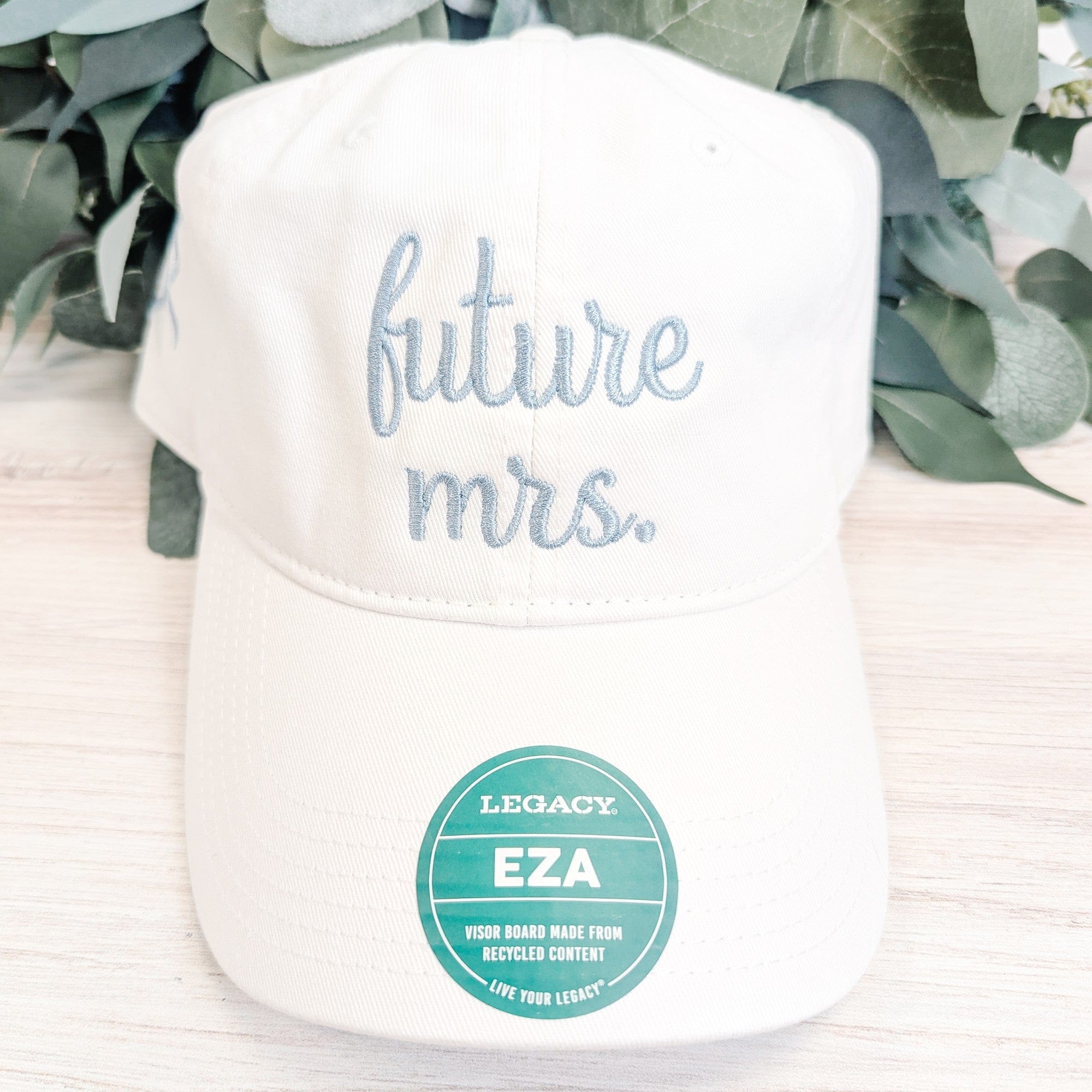 A white cotton blend baseball cap features light blue embroidered text, serving as a personalized bridal accessory.