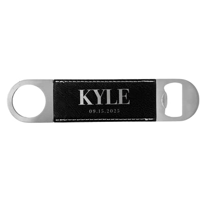 A rectangular silver-colored metal bottle opener featuring a black textured faux leather insert with white stitching, suitable as a personalized wedding favor or gift.
