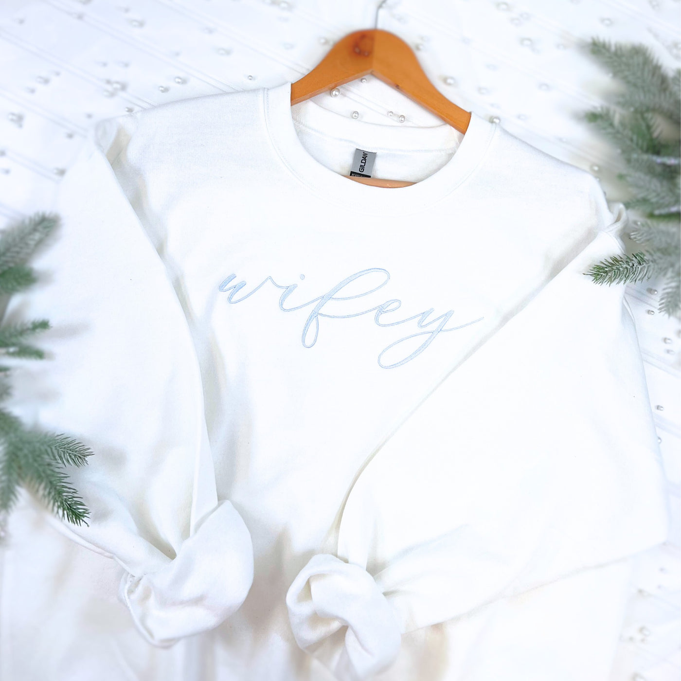 A soft white crewneck sweatshirt features delicate light blue script embroidery, ideal for bridal events or as a comfortable gift.