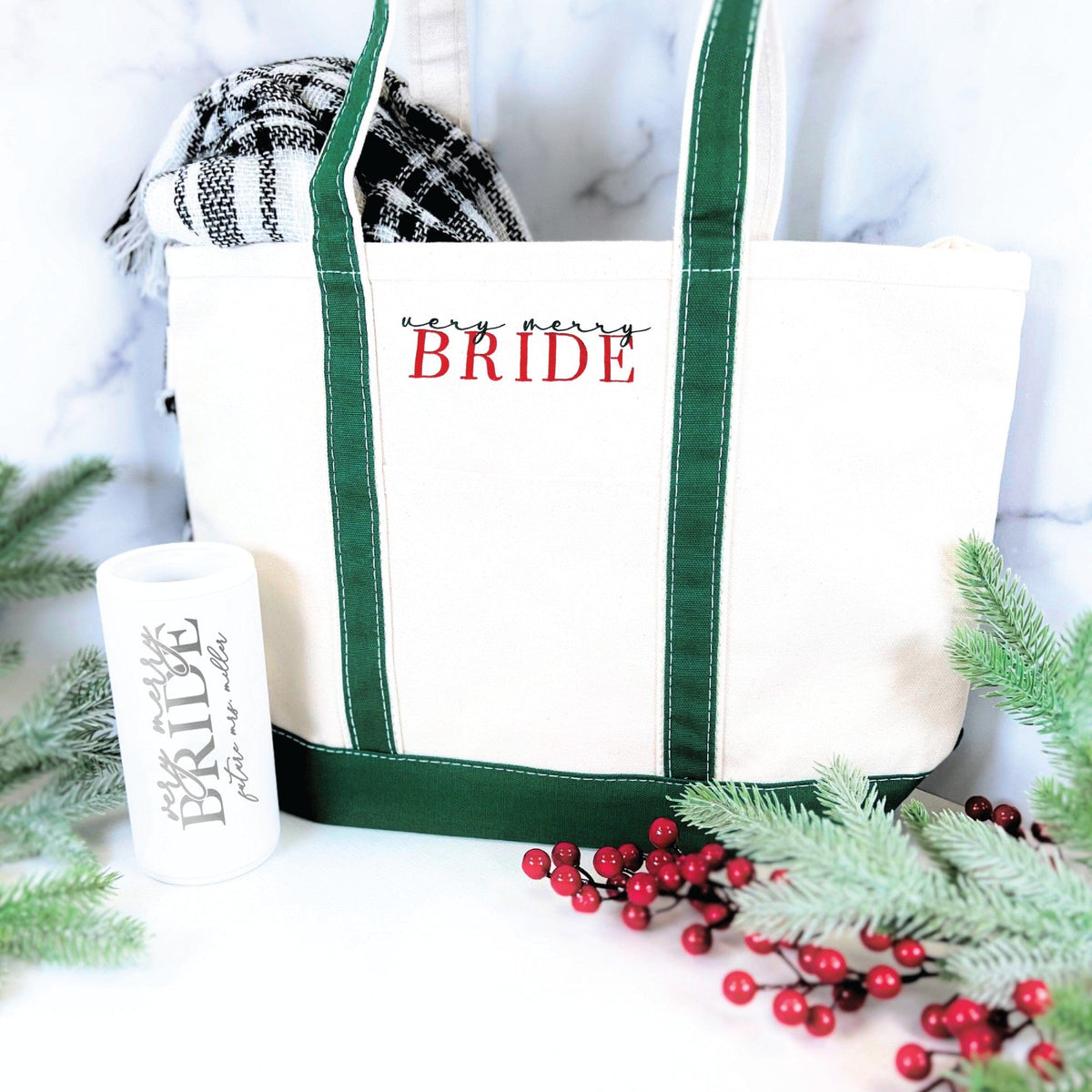 A festive canvas tote bag with deep green straps and base is paired with a matching white insulated tumbler, presented as a charming winter-themed wedding or bridal shower gift set.
