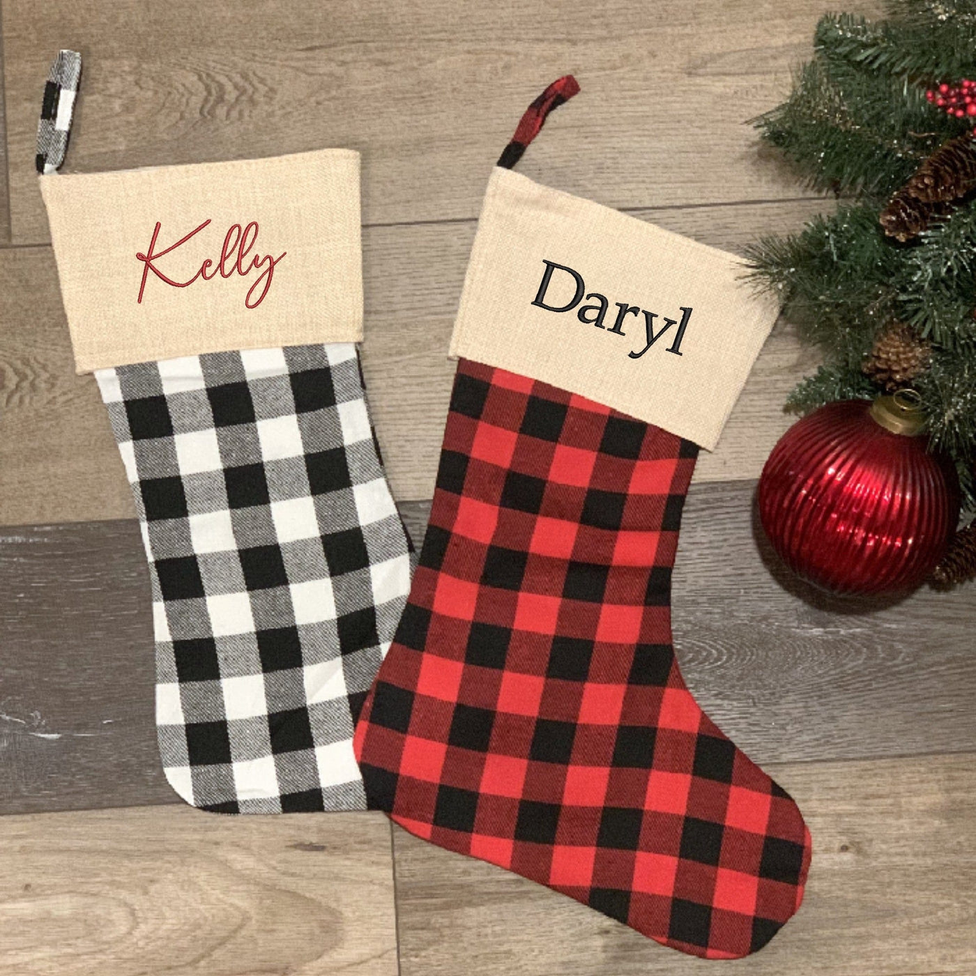 Two personalized fabric Christmas stockings, one in black and white buffalo plaid and the other in red and black buffalo plaid, each with a rustic burlap cuff, designed for festive holiday decor.