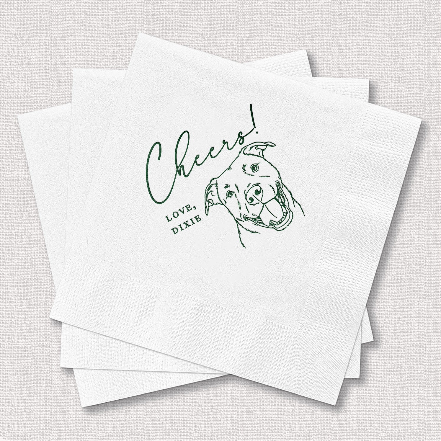A stack of white, textured disposable cocktail napkins featuring a green line art illustration of a smiling dog, designed for a personalized party or celebration.