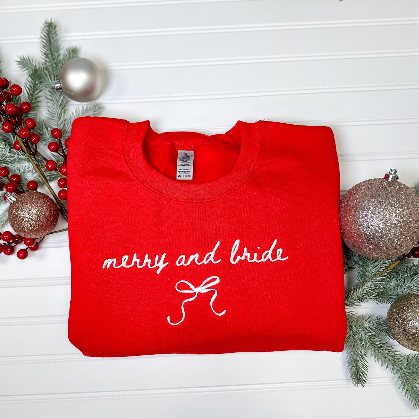 A vibrant red crewneck sweatshirt featuring elegant white embroidery and a bow design, perfect for a festive holiday bridal celebration.