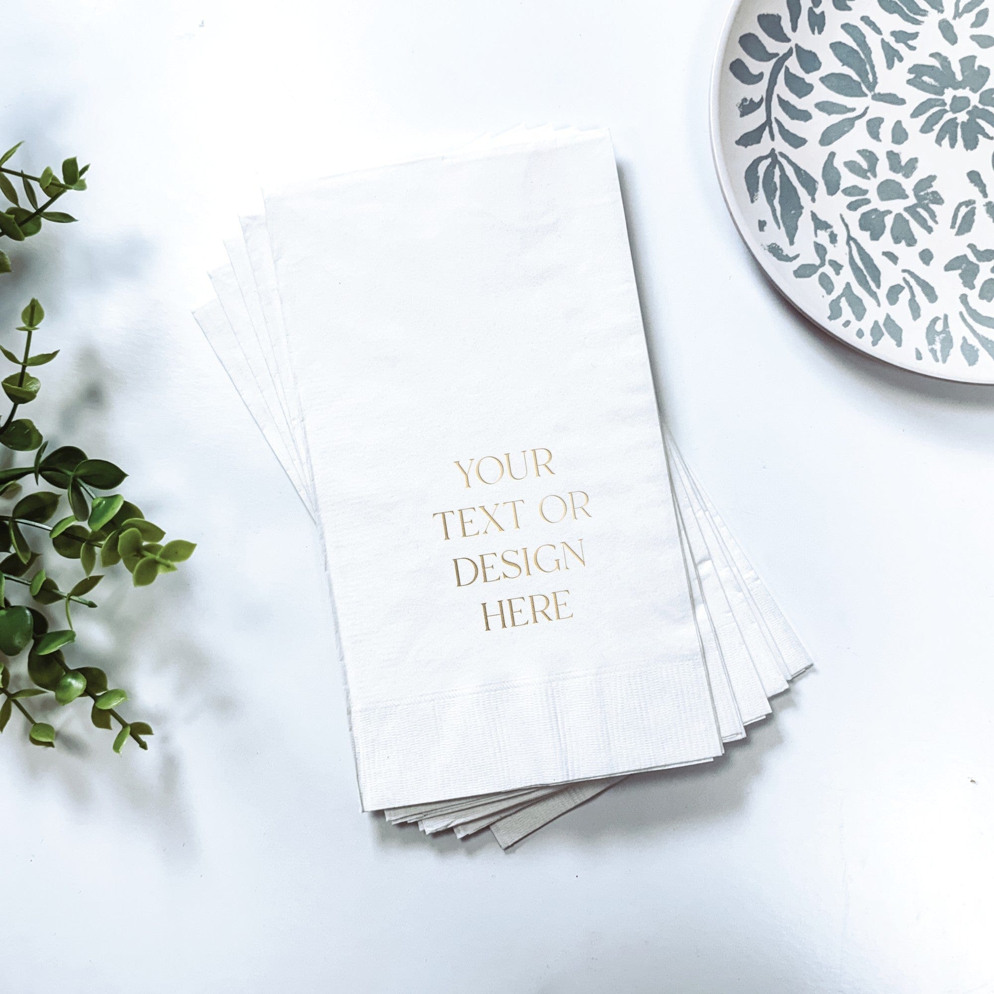 A stack of elegant white folded paper guest towels with customizable metallic gold printing, suitable for a wedding, bridal shower, or special event.