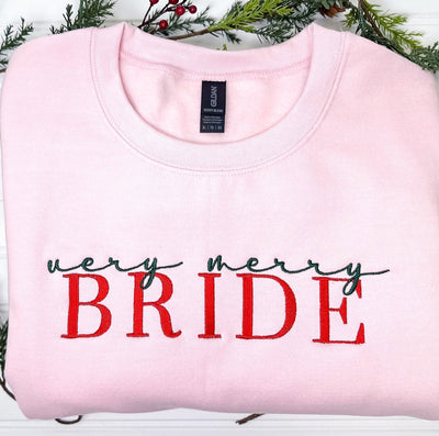 A personalized light pink crewneck sweatshirt featuring vibrant green and red festive embroidery, suitable for bridal or pre-wedding holiday events.