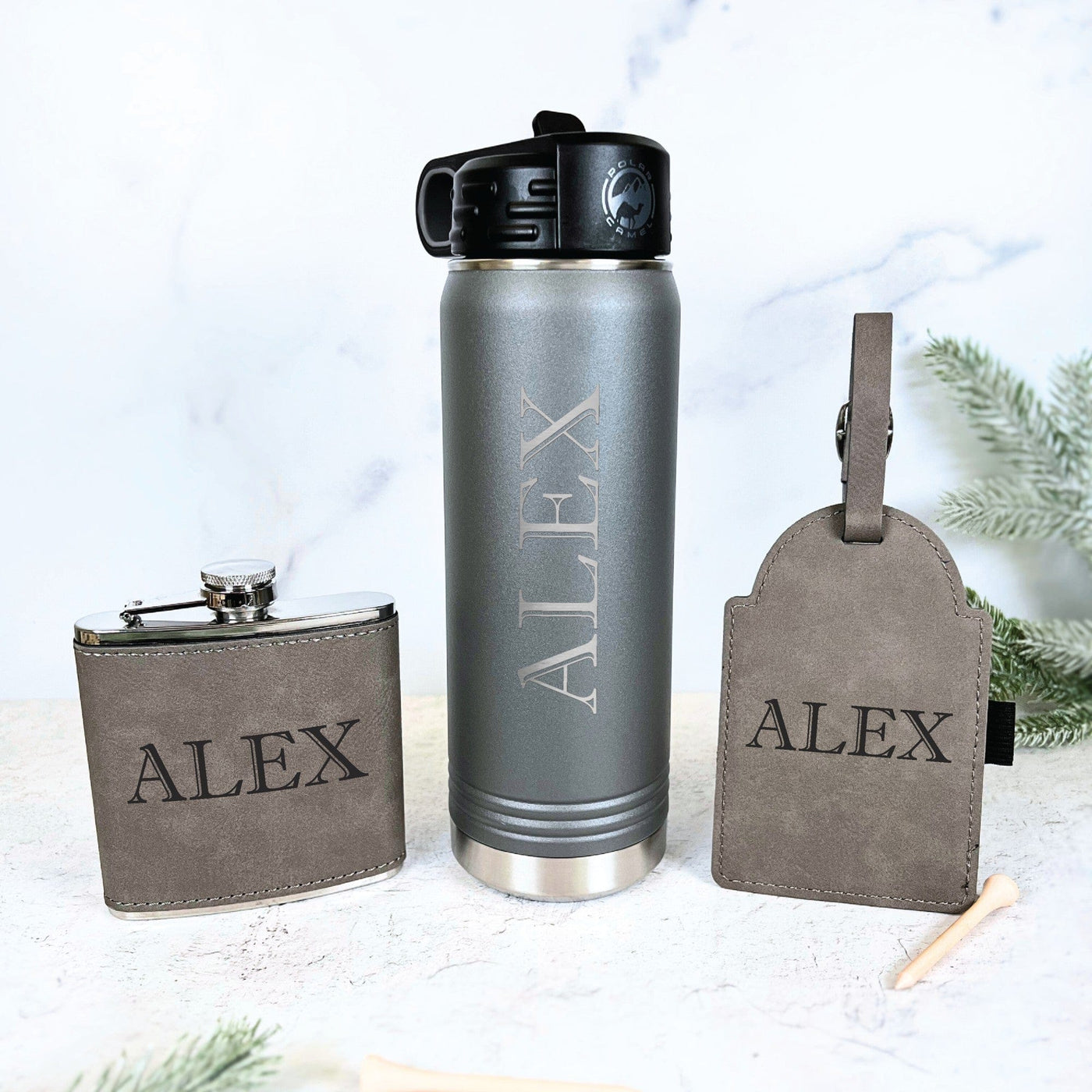 A personalized grey and silver gift set featuring a faux suede covered hip flask, an insulated water bottle, and a matching faux suede luggage tag, suitable for a wedding party.