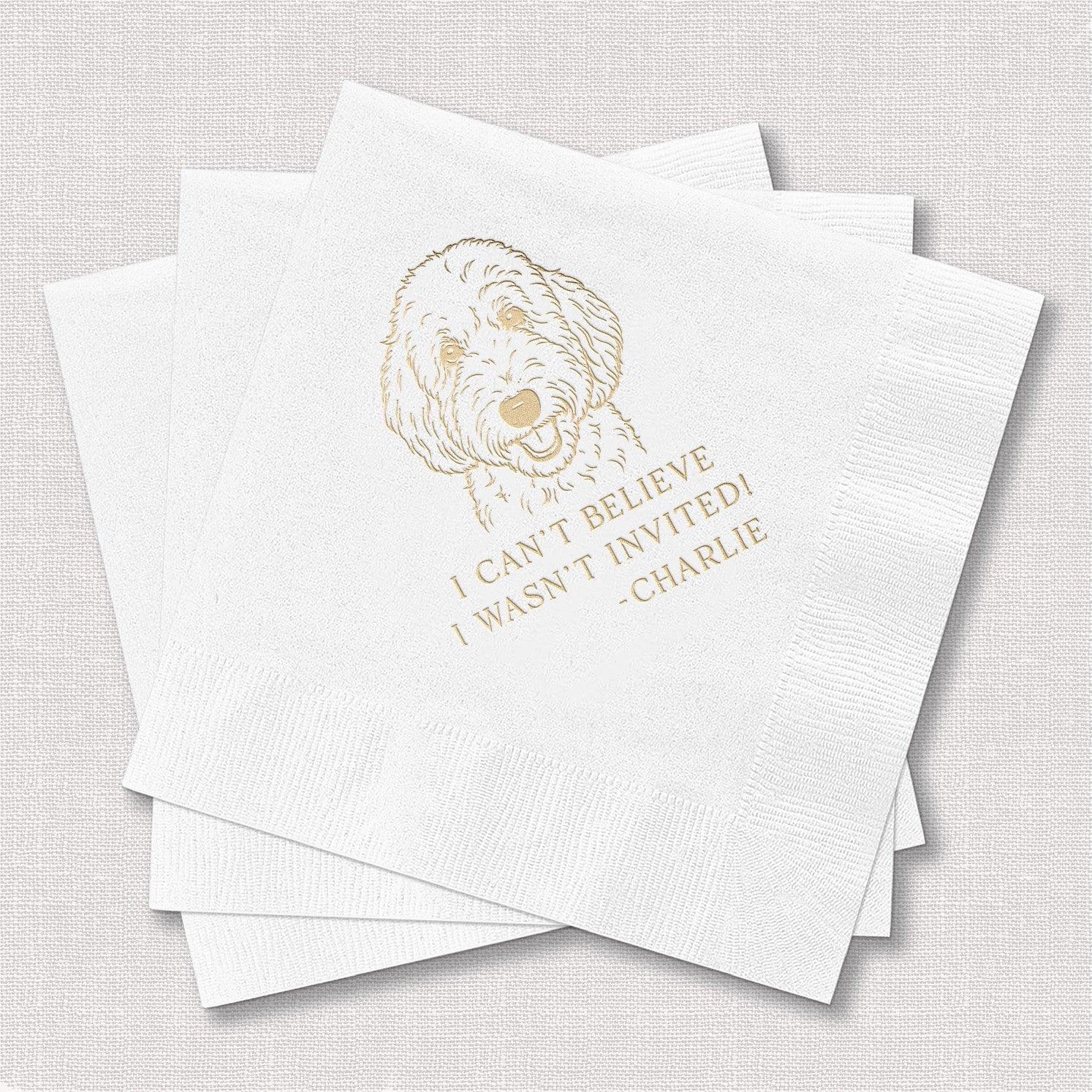 A stack of three textured white paper cocktail napkins, with the top napkin displaying a custom gold foil illustration of a dog's head, perfect for personalized event decor.