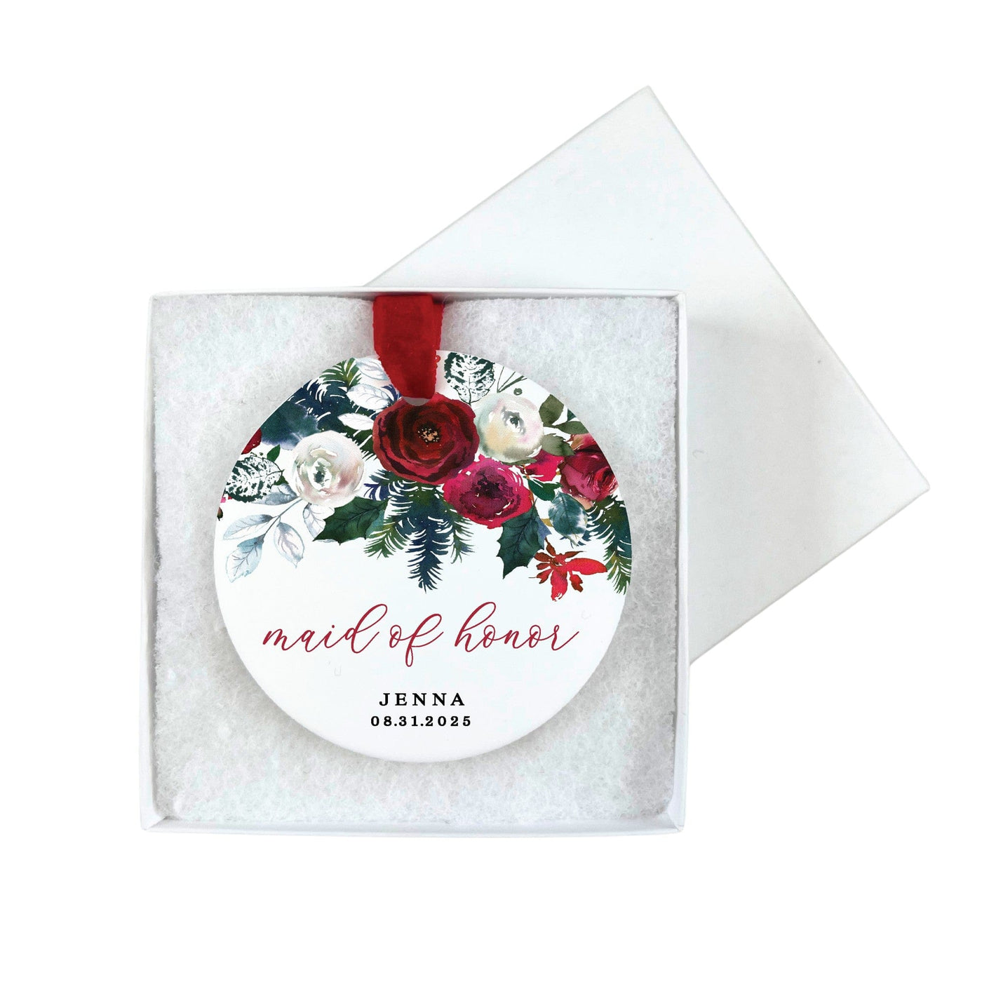 A round ceramic ornament featuring a vibrant winter floral design in rich reds, whites, and deep greens, suspended by a red ribbon and presented in a white gift box, ideal for a wedding party.