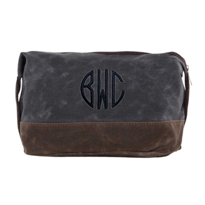 A personalized two-tone waxed canvas toiletry bag in dark grey and brown, featuring an embroidered circular monogram design and a top zipper closure, perfect for travel essentials or as a wedding party gift.