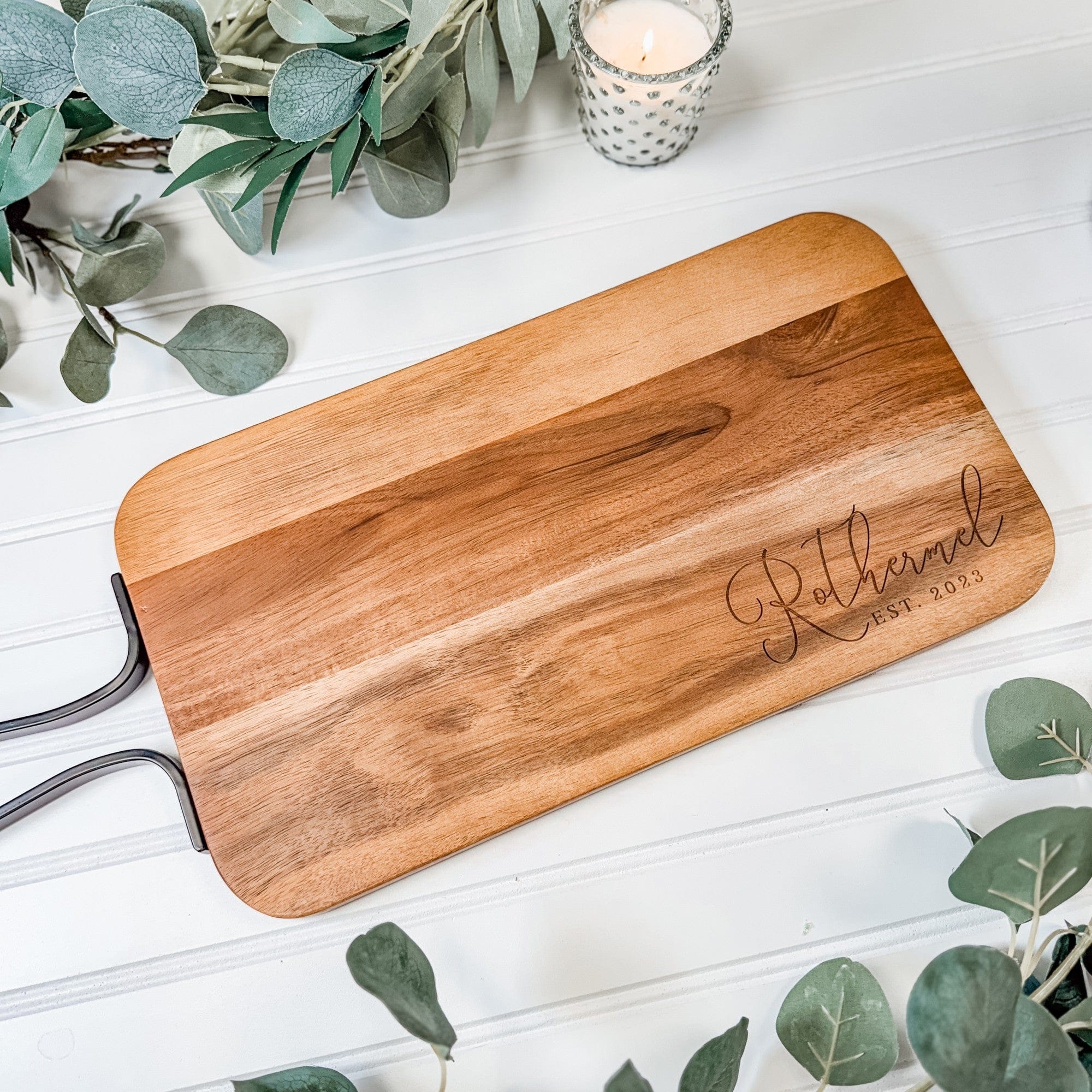 An oblong personalized wooden serving board with sleek black metal handles, suitable as a wedding or special event decor item.